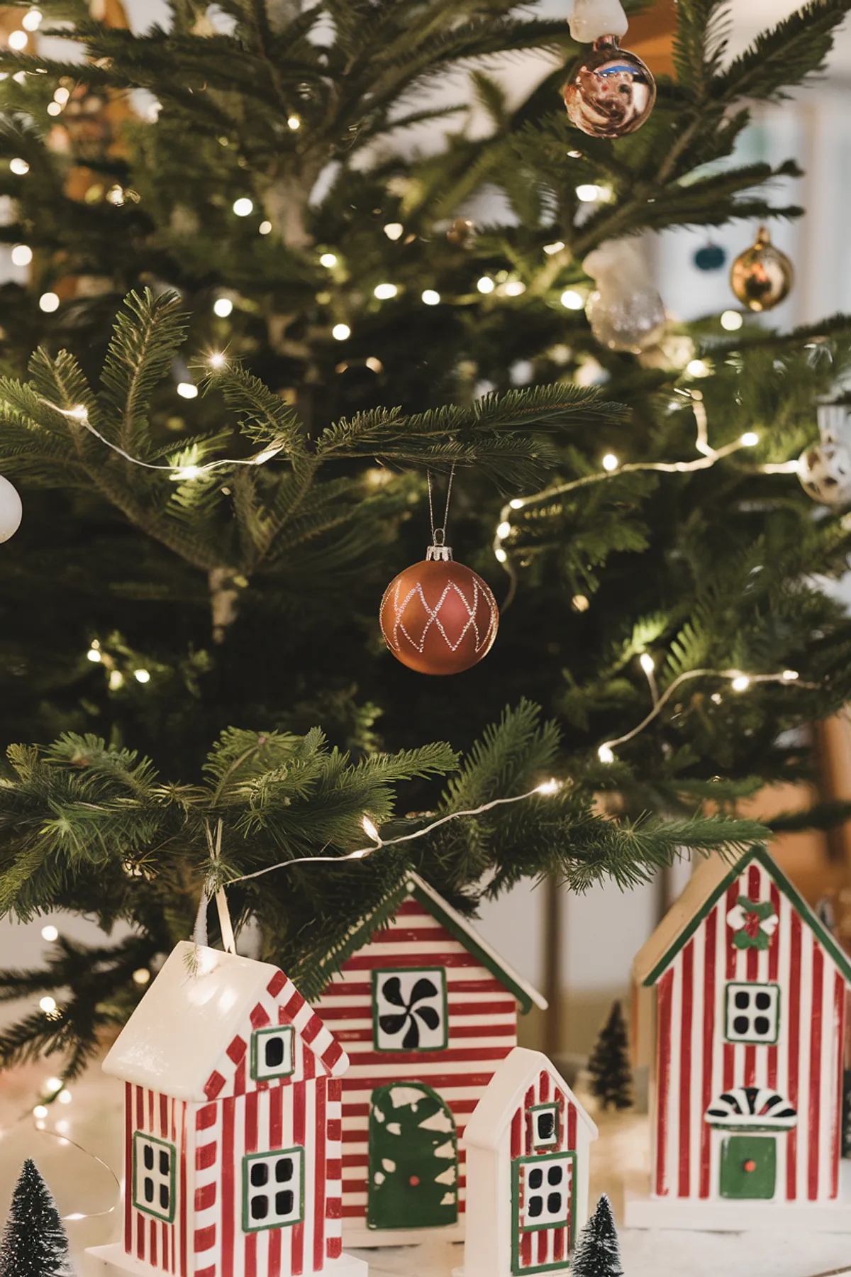 Festive scene featuring a decorated Christmas tree with red and gold ornaments alongside striped wooden houses and miniature trees.