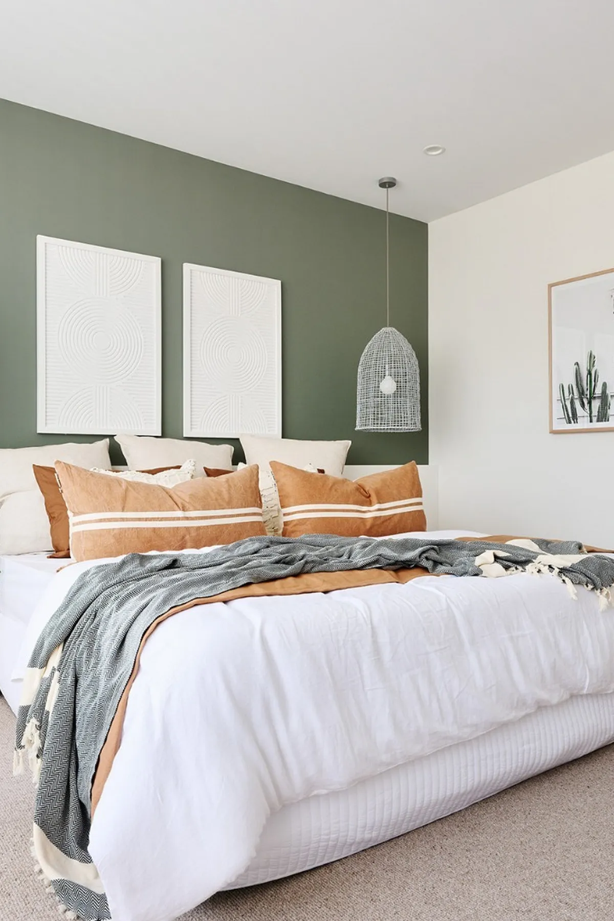A stylish bedroom featuring a green accent wall, rust-colored bedding, geometric art, woven pendant lights, and natural elements.