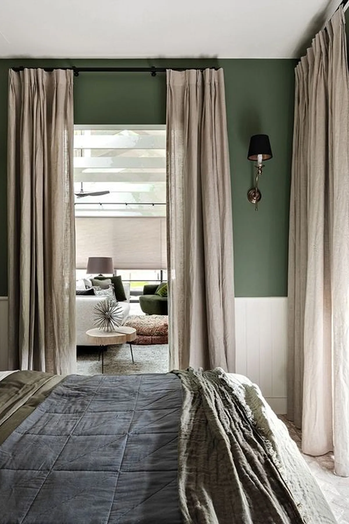 A cozy green bedroom featuring a large abstract painting, neutral pillows, floor-to-ceiling windows, and a beige curtain for natural light.