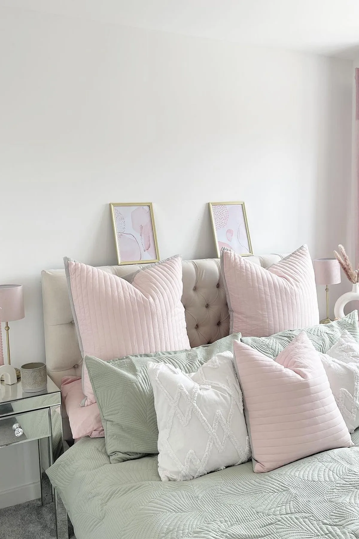 A tranquil bedroom featuring pastel bedding, abstract art, mirrored nightstand, pink curtains, and natural light creating a calm ambiance.
