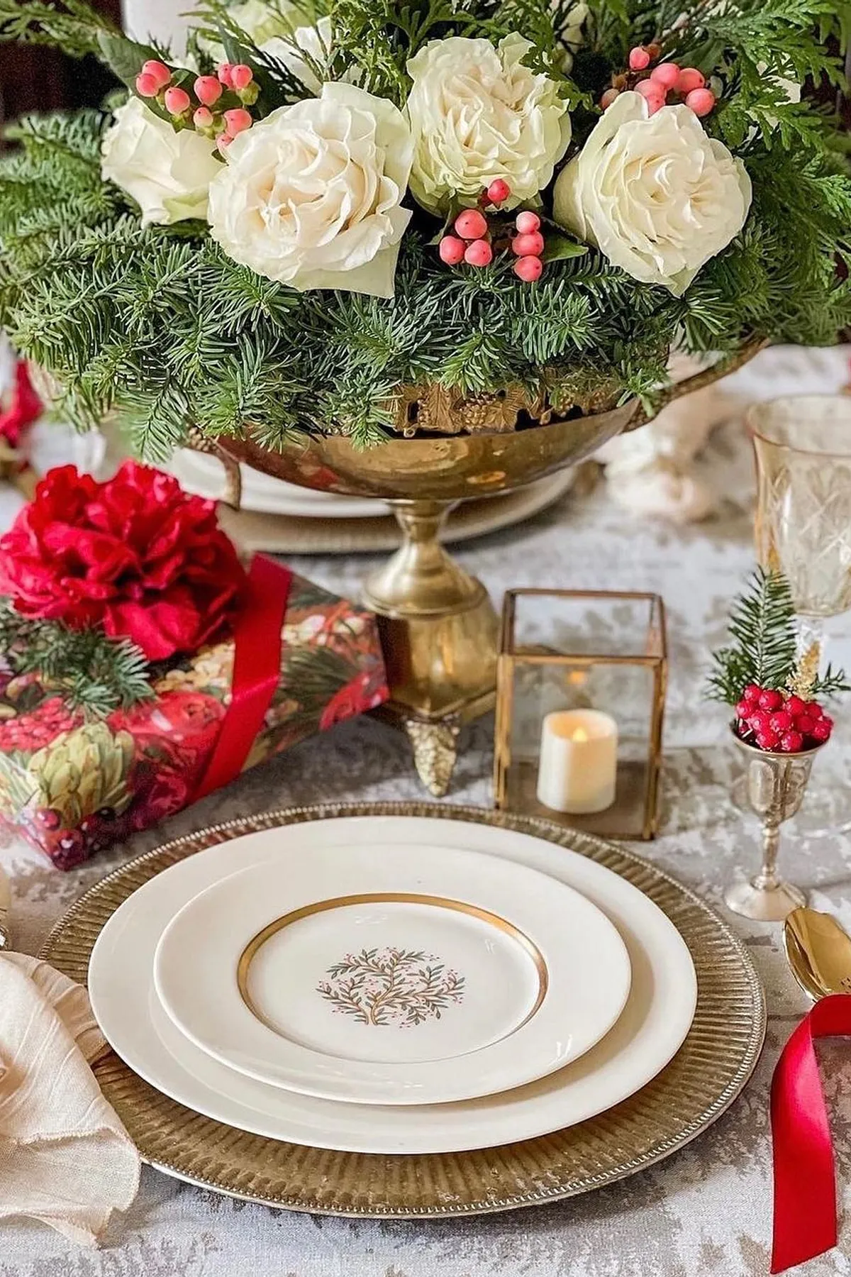 Festive dining table set with floral centerpiece, elegant plates, a gift, and candles for an inviting ambiance.