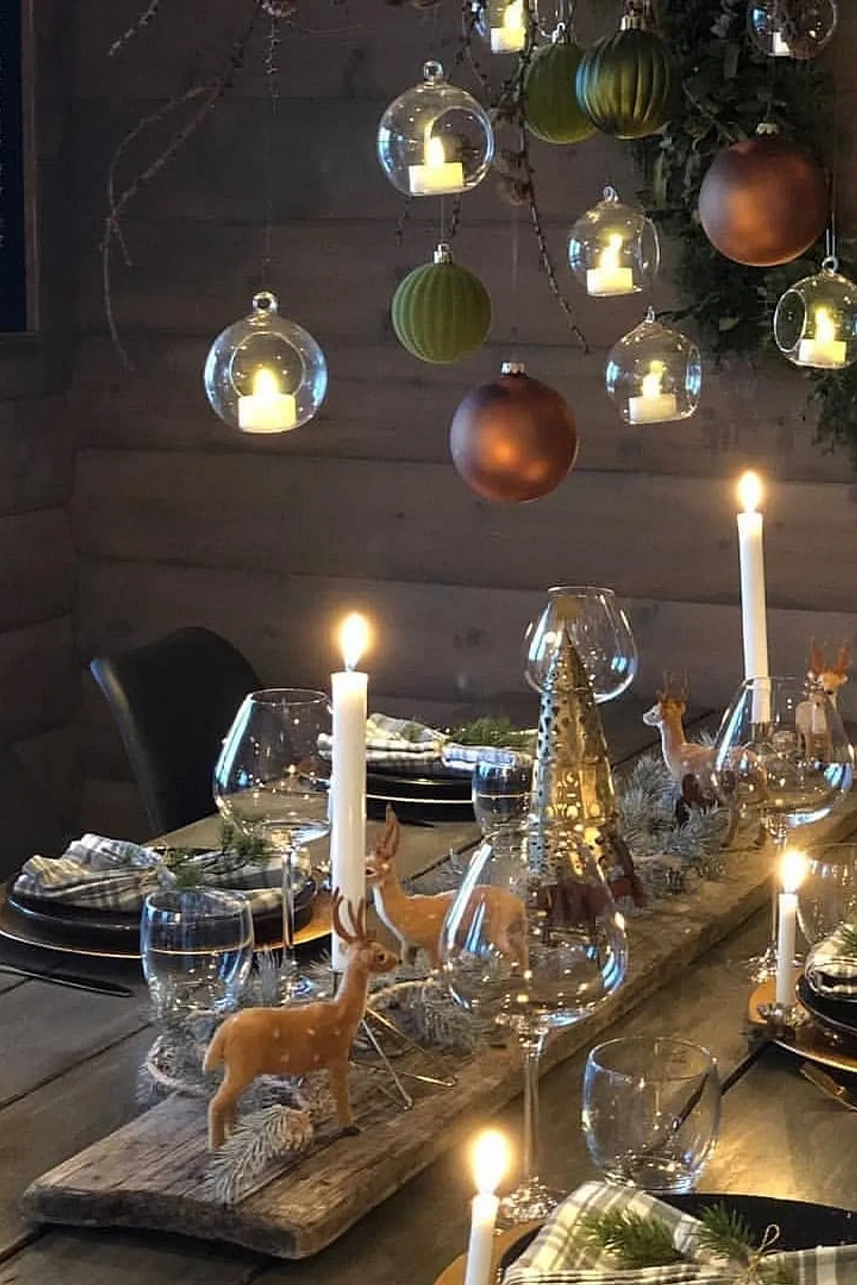 Cozy dining setting with candlelight, glass ornaments, reindeer figurines, set table, and warm wooden backdrop for a festive occasion.
