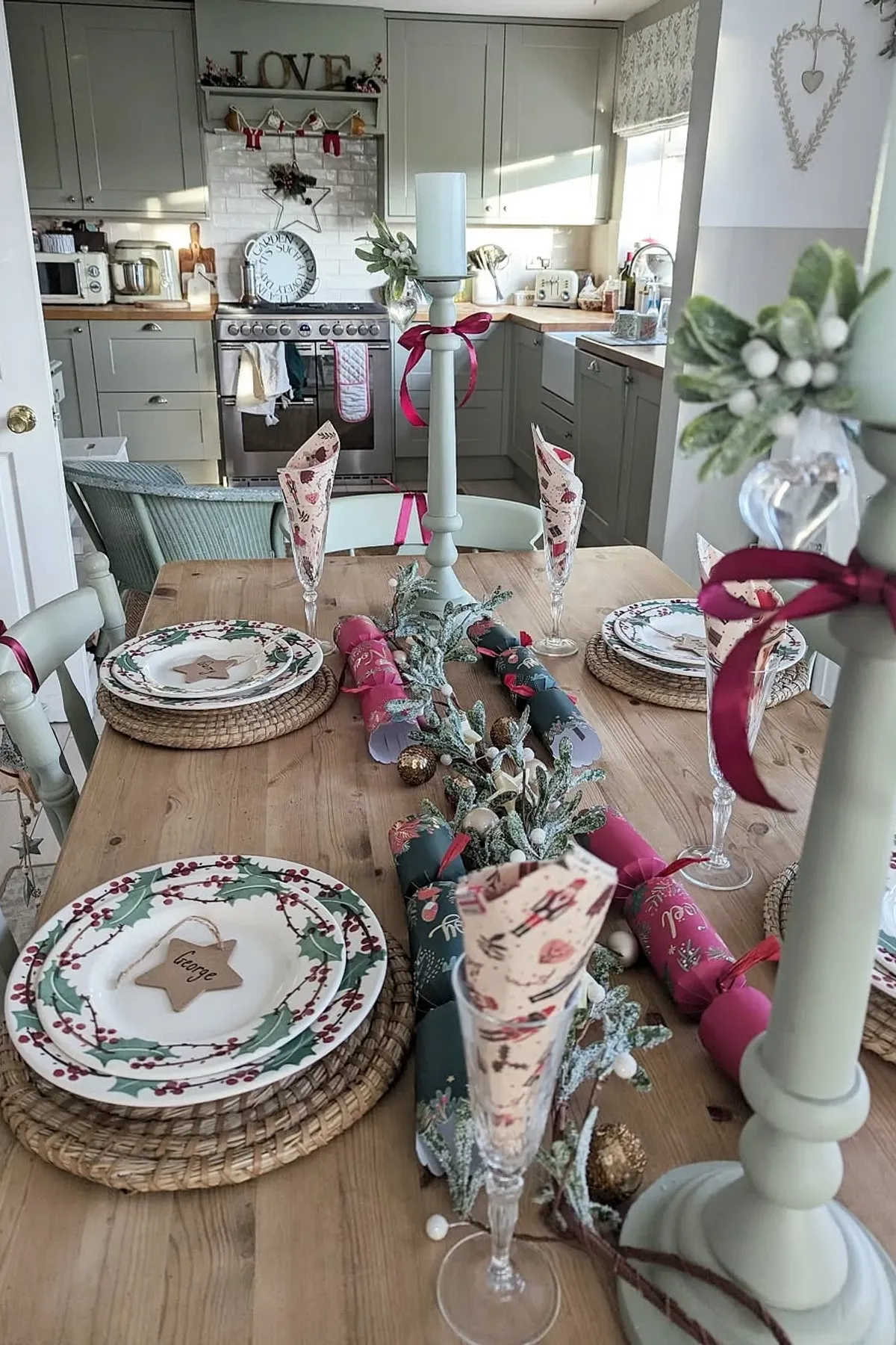 Cozy festive kitchen with wooden table, holiday plates, candles, greenery, and decorative garlands creating a warm atmosphere for gatherings.