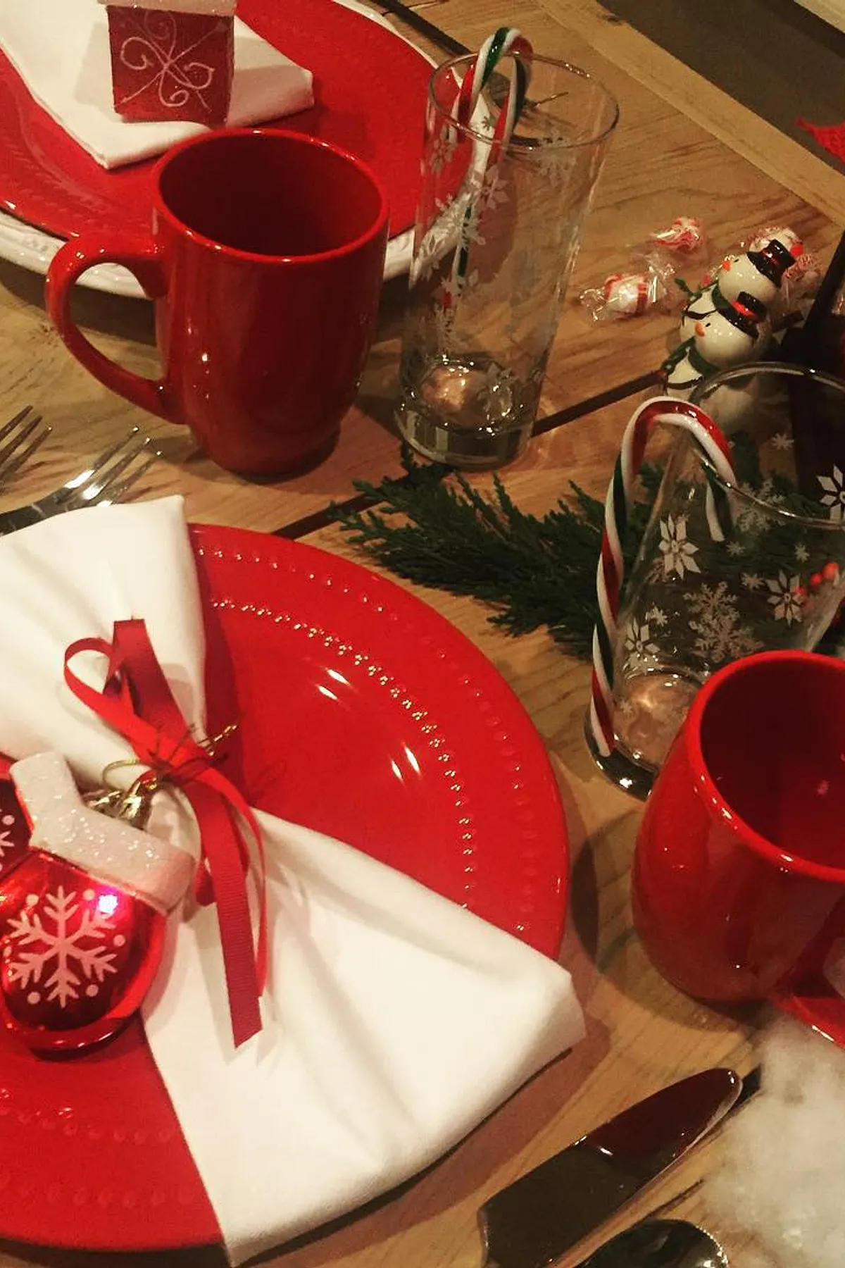 Festive holiday table with red mugs, white plates, mitten napkin holders, snowflake glasses, and a lantern featuring candy canes.