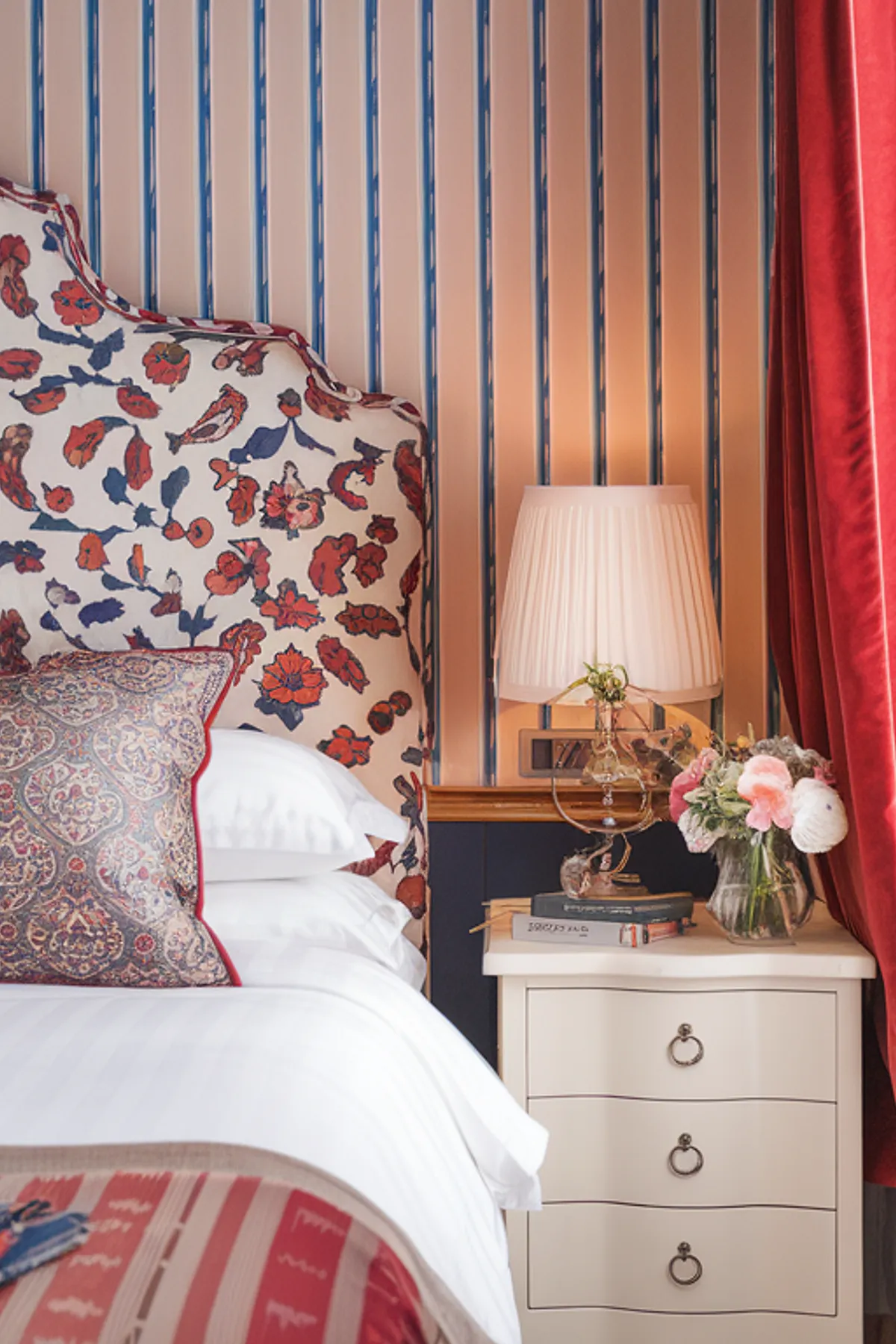 Luxurious bedroom with floral headboard, striped walls, and deep red curtain.