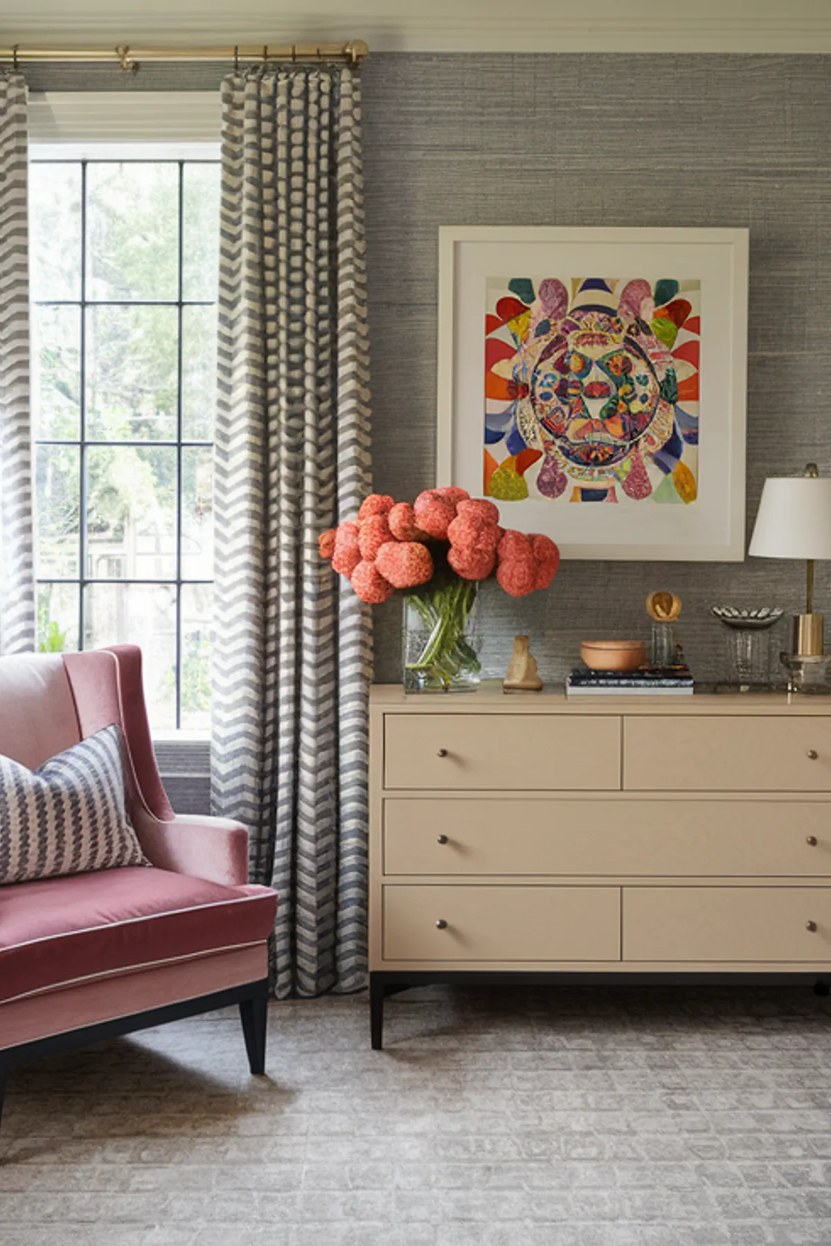 Bedroom with gray patterned wallpaper, zigzag headboard, chevron curtains, colorful artwork, and pink chair.