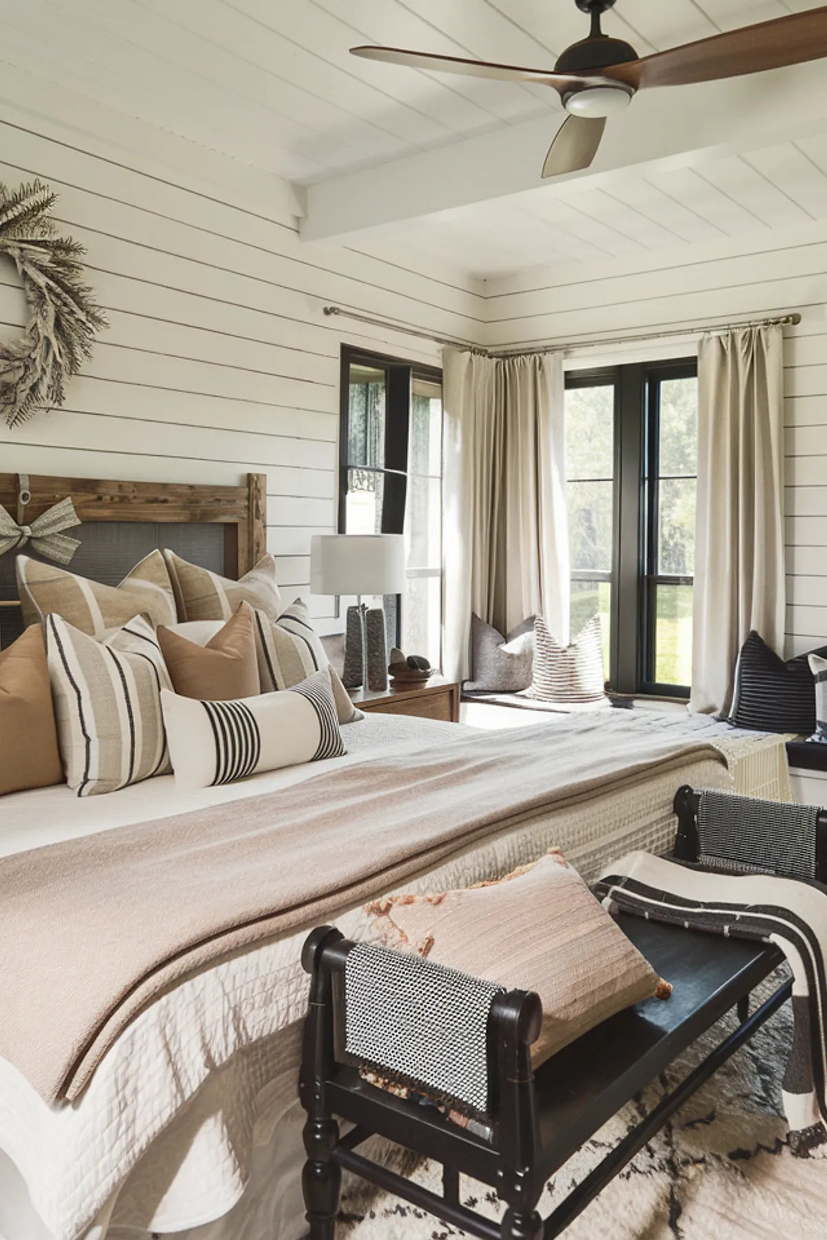 Bedroom with neutral-toned pillows, rustic headboard, and a decorative dried leaf wreath.