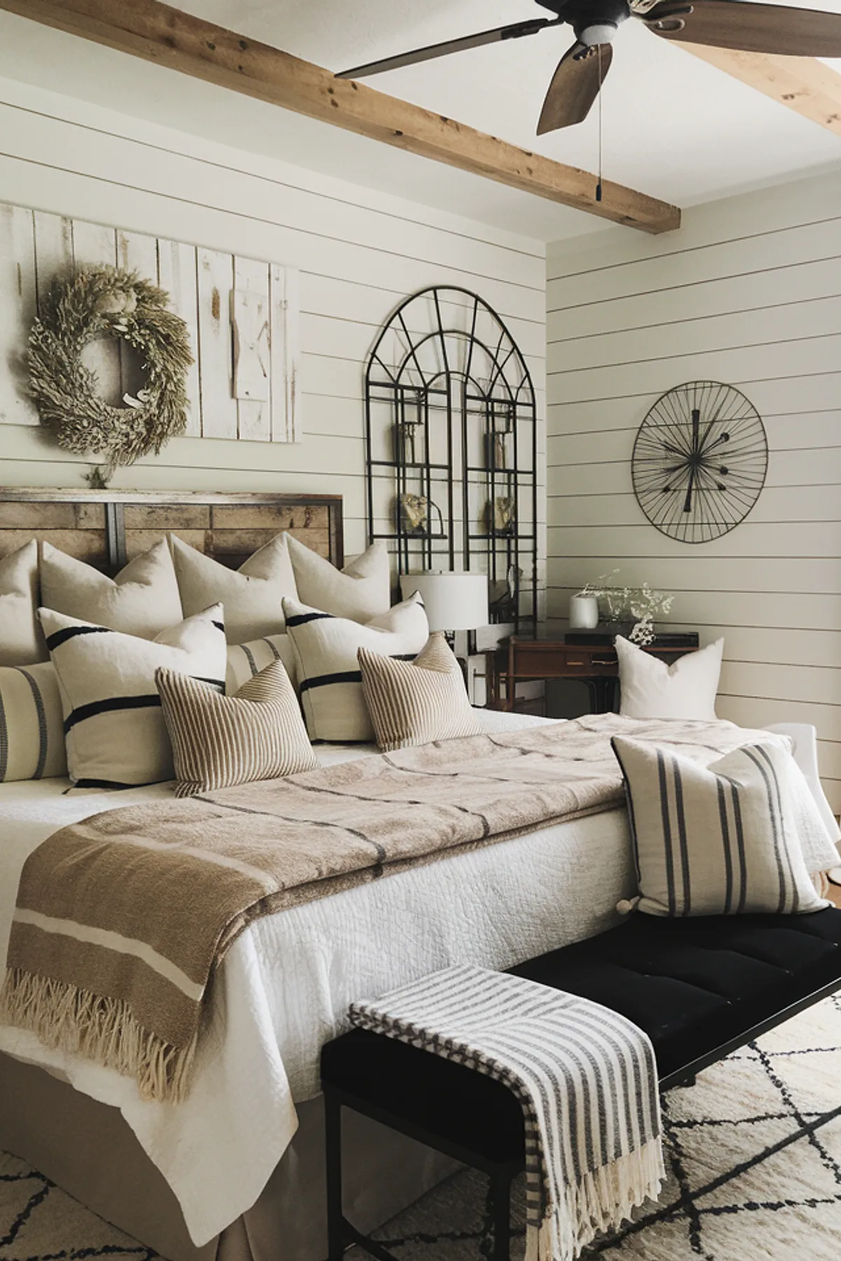 Bedroom with a beige blanket, wooden beams, decorative wreath, and geometric rug.