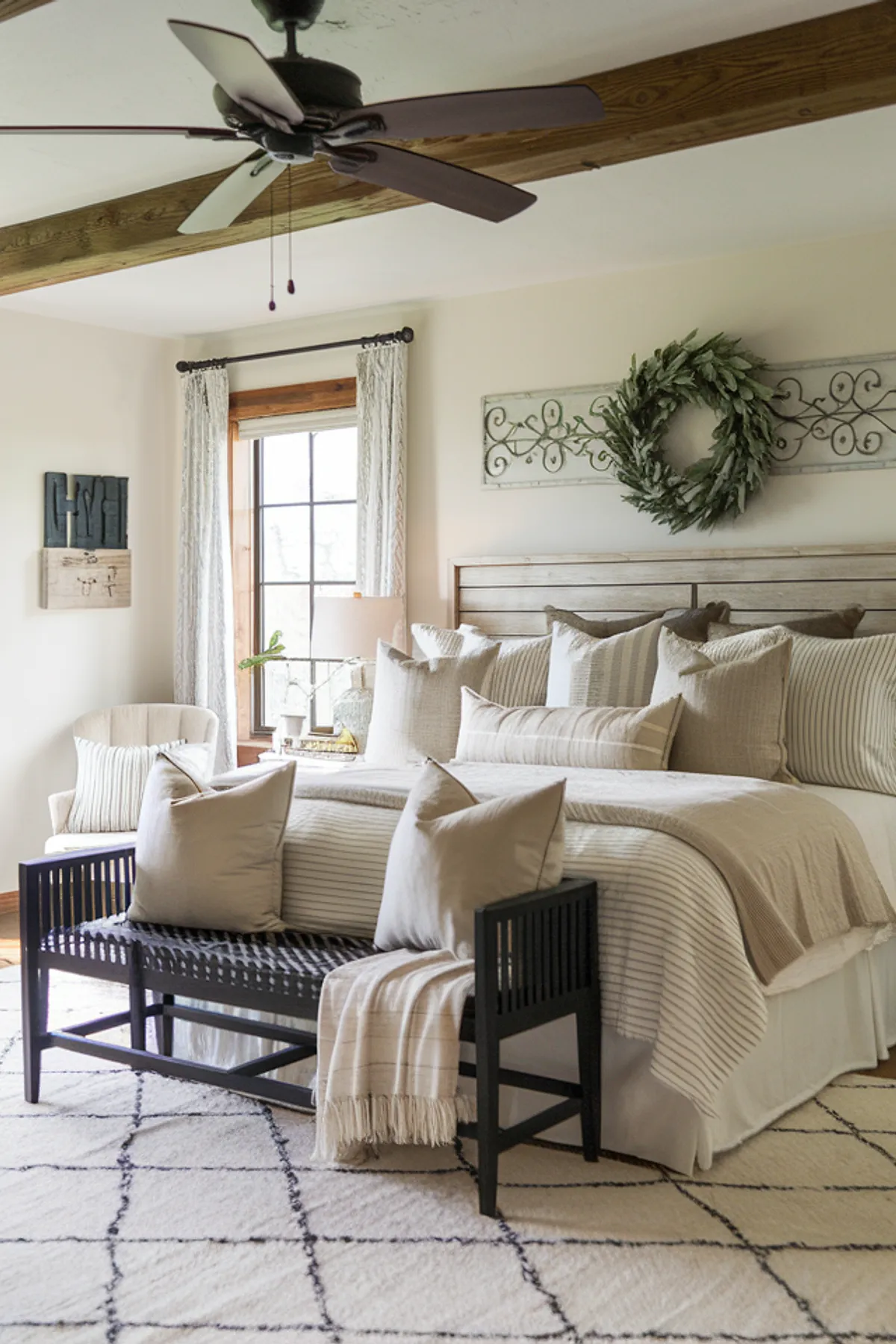 Bedroom with striped bedding, decorative metal wall piece, and wooden chair near window.