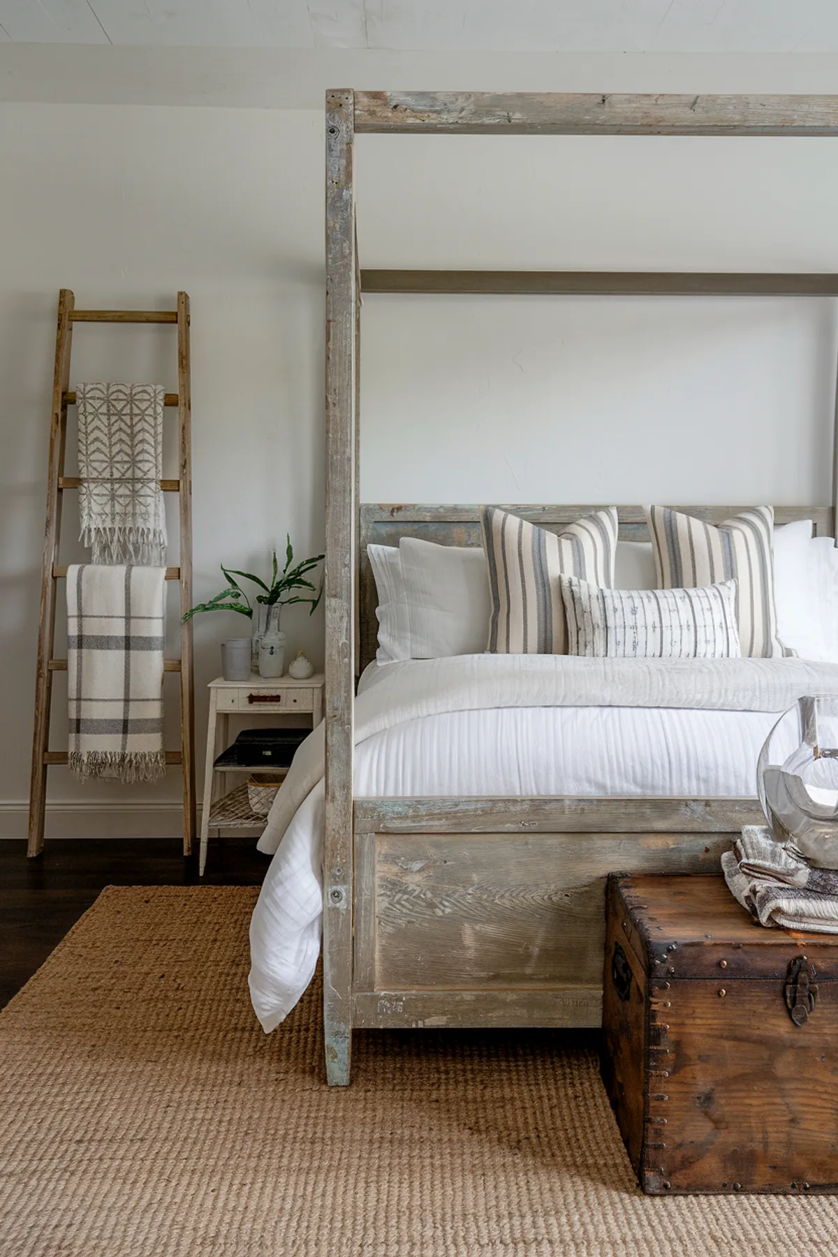 Serene bedroom with rustic wooden bed, striped pillows, and geometric blanket on ladder.