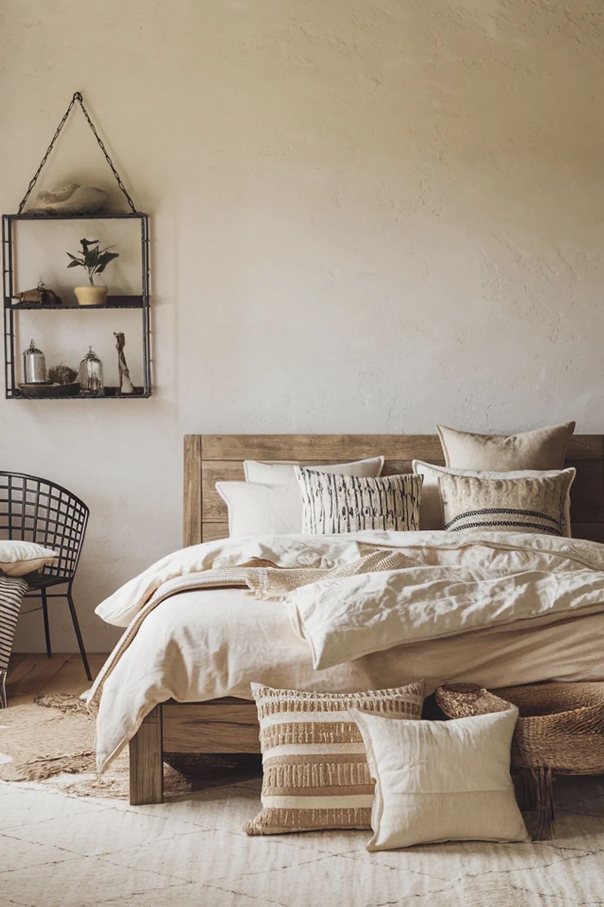 Bedroom with wooden bed, neutral bedding, metal shelf with plants, and geometric rug.