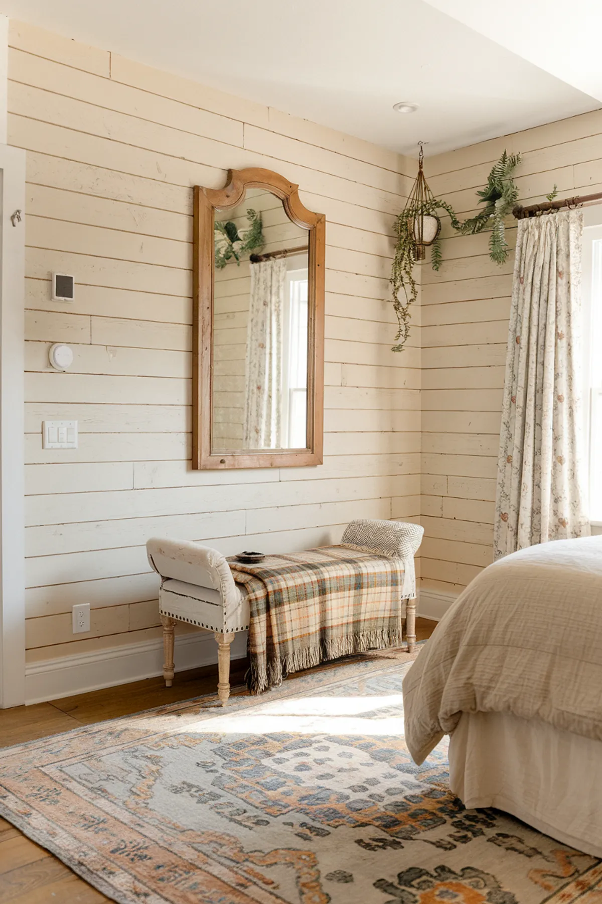 Bedroom with wooden bed, beige linens, floral curtains, and a patterned rug.
