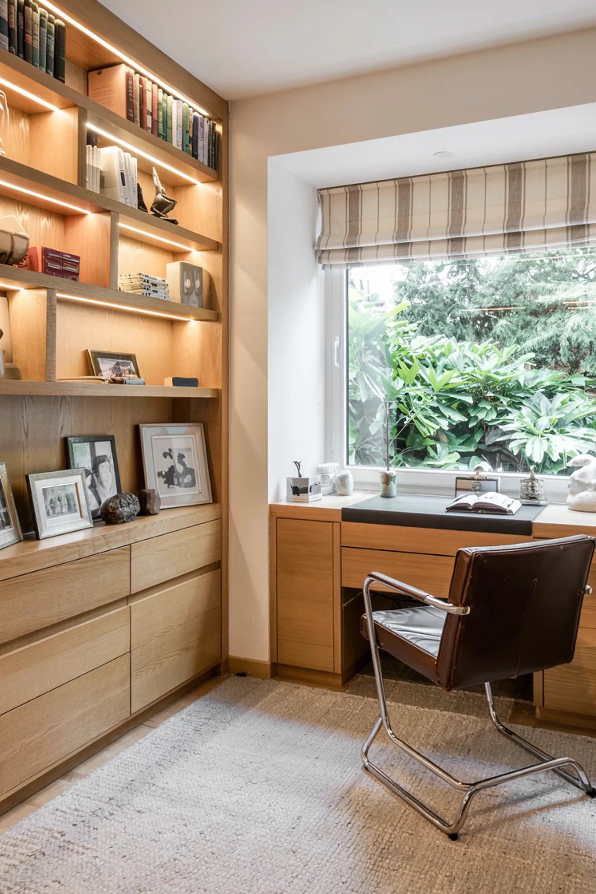 Home office featuring wooden shelves, large window with greenery view, modern desk, and cozy seating.
