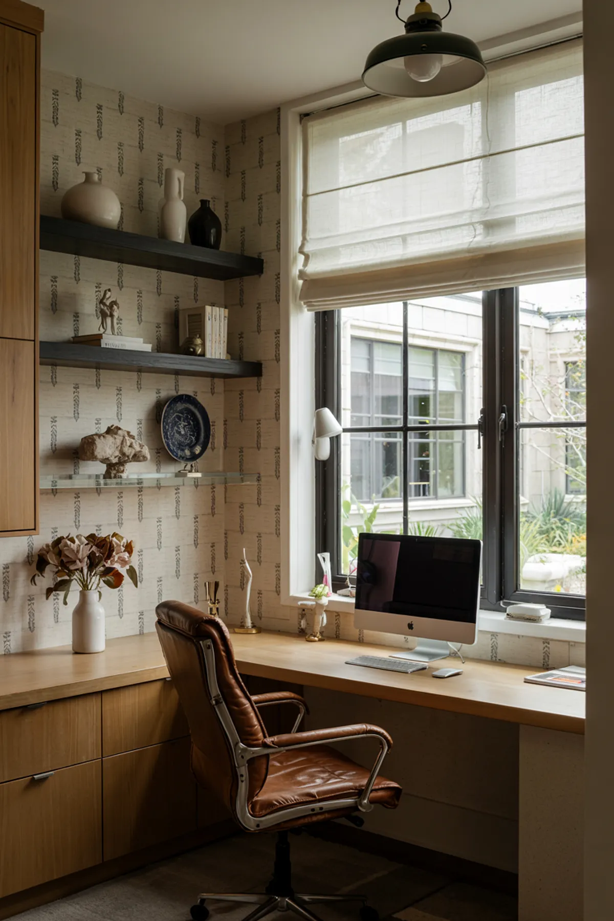 Home office featuring wooden shelves, decorative vases, an iMac, large window with greenery view, and stylish chair.