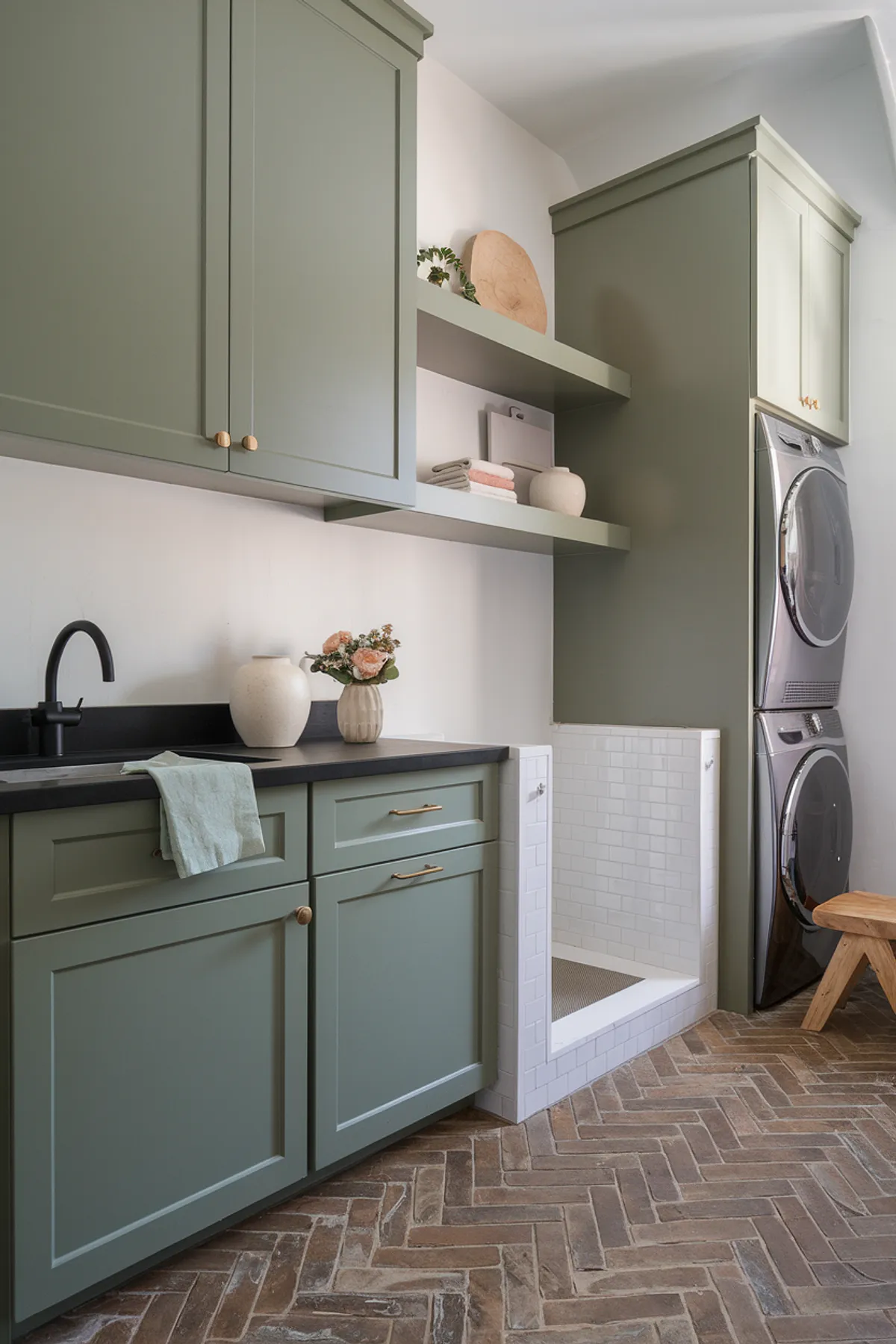 A stylish laundry room featuring earthy green cabinets and herringbone flooring.