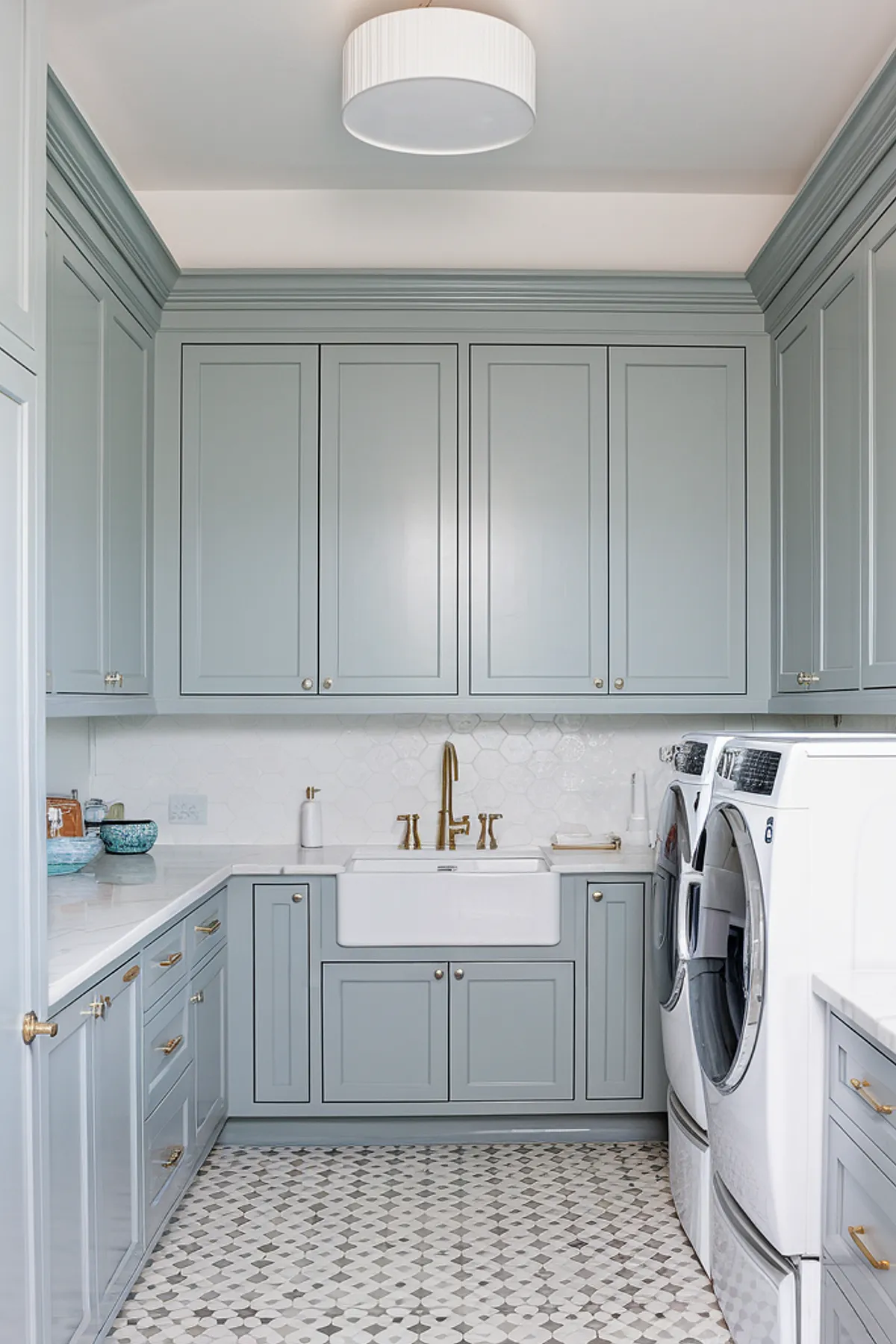 A stylish laundry room featuring soft blue cabinets and elegant gold fixtures.