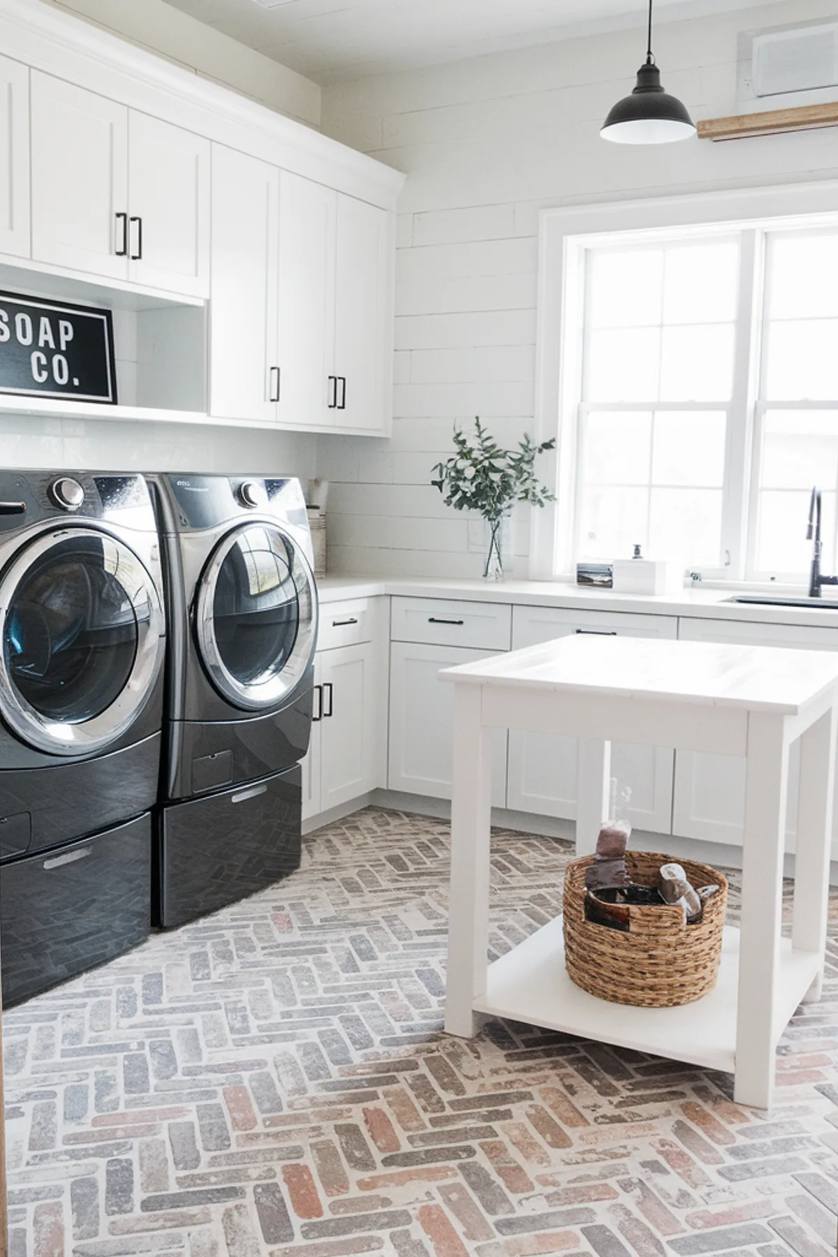 A modern farmhouse laundry room featuring black appliances and herringbone flooring.