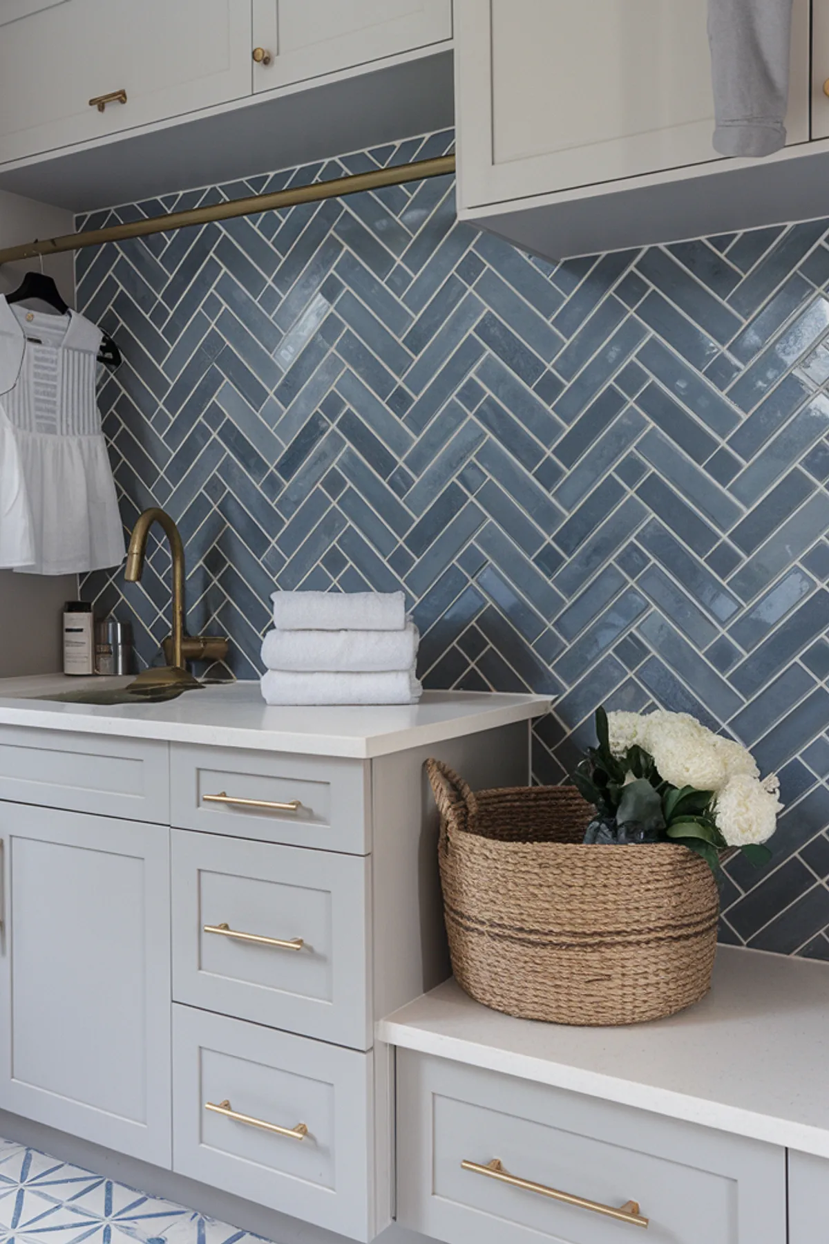 A stylish laundry room featuring a blue herringbone tile backsplash and gray cabinetry.