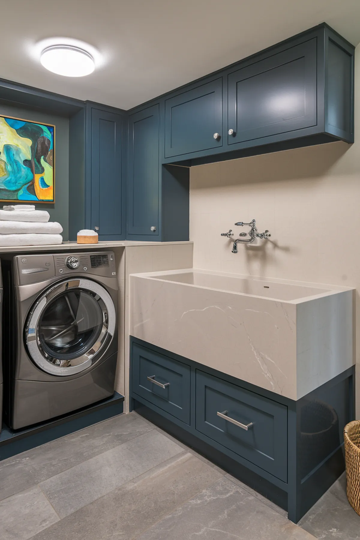 A modern laundry room featuring navy blue cabinets and a neutral stone sink.