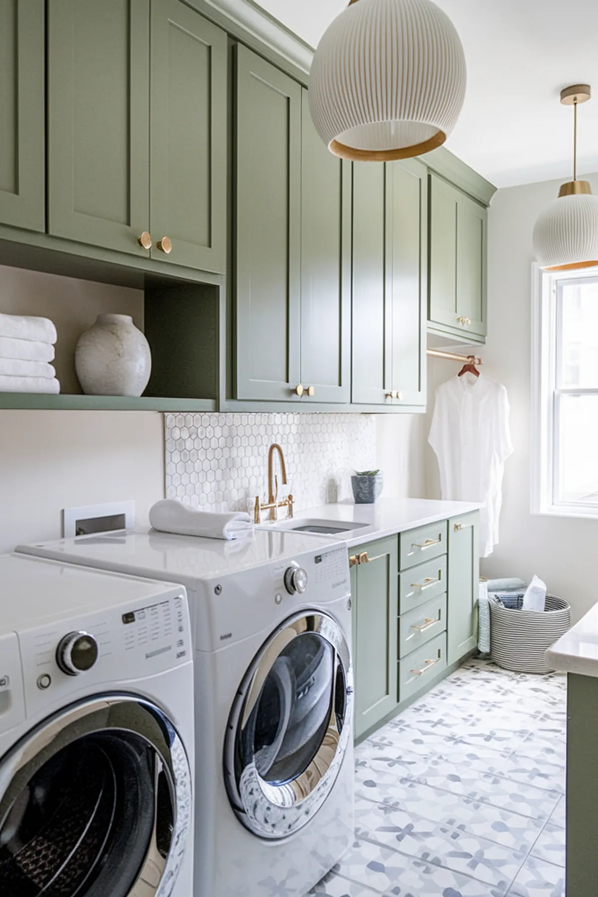 A stylish laundry room with green cabinets, brass fixtures, and an elegant backsplash.