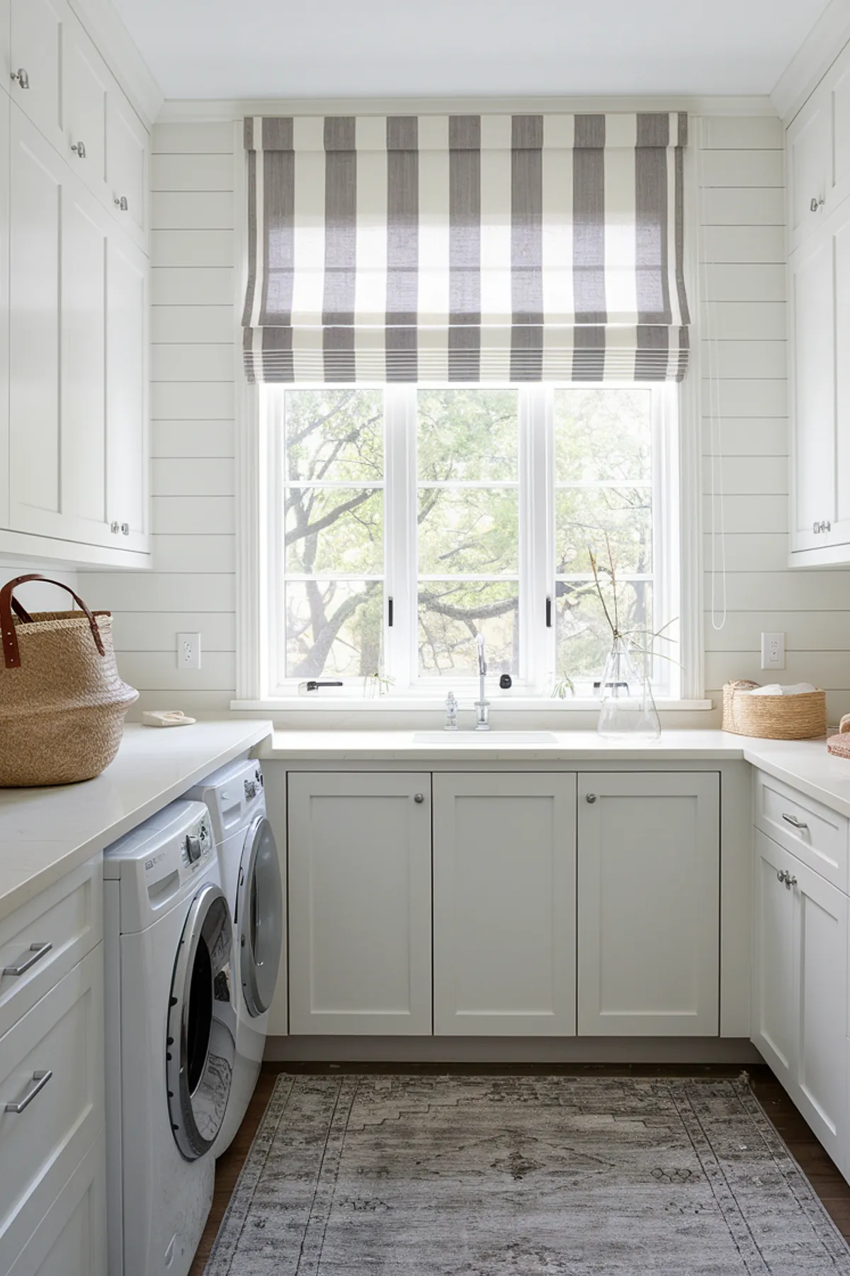 A bright laundry room featuring white cabinets, a striped window treatment, and modern appliances.