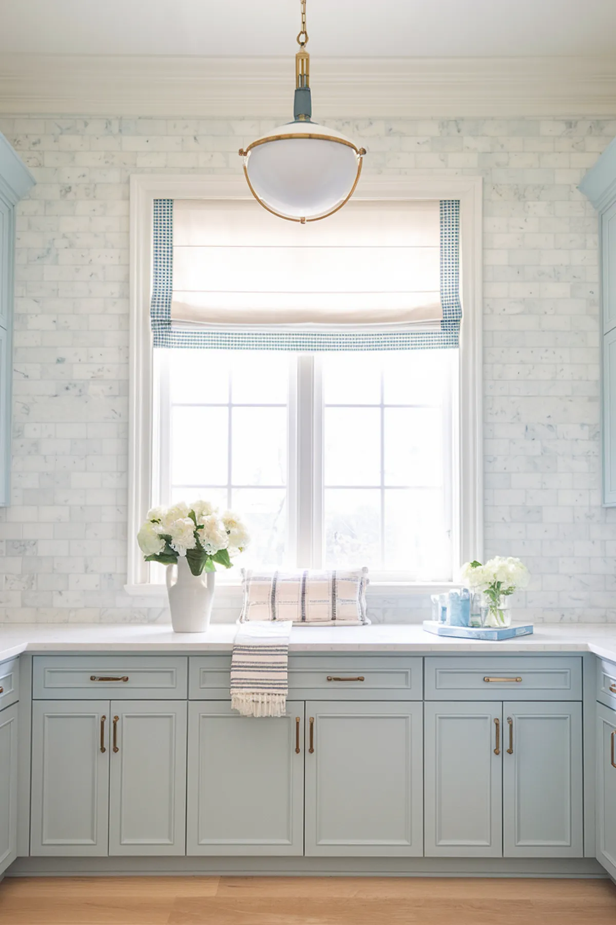 A serene laundry room with light blue cabinets and a marble backsplash.