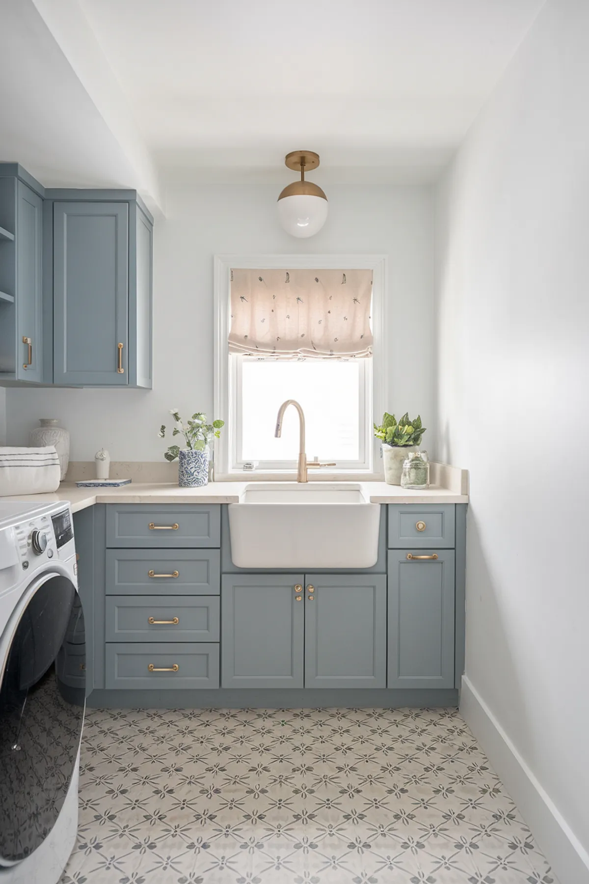 A charming laundry room featuring blue cabinets, a farmhouse sink, and patterned flooring.