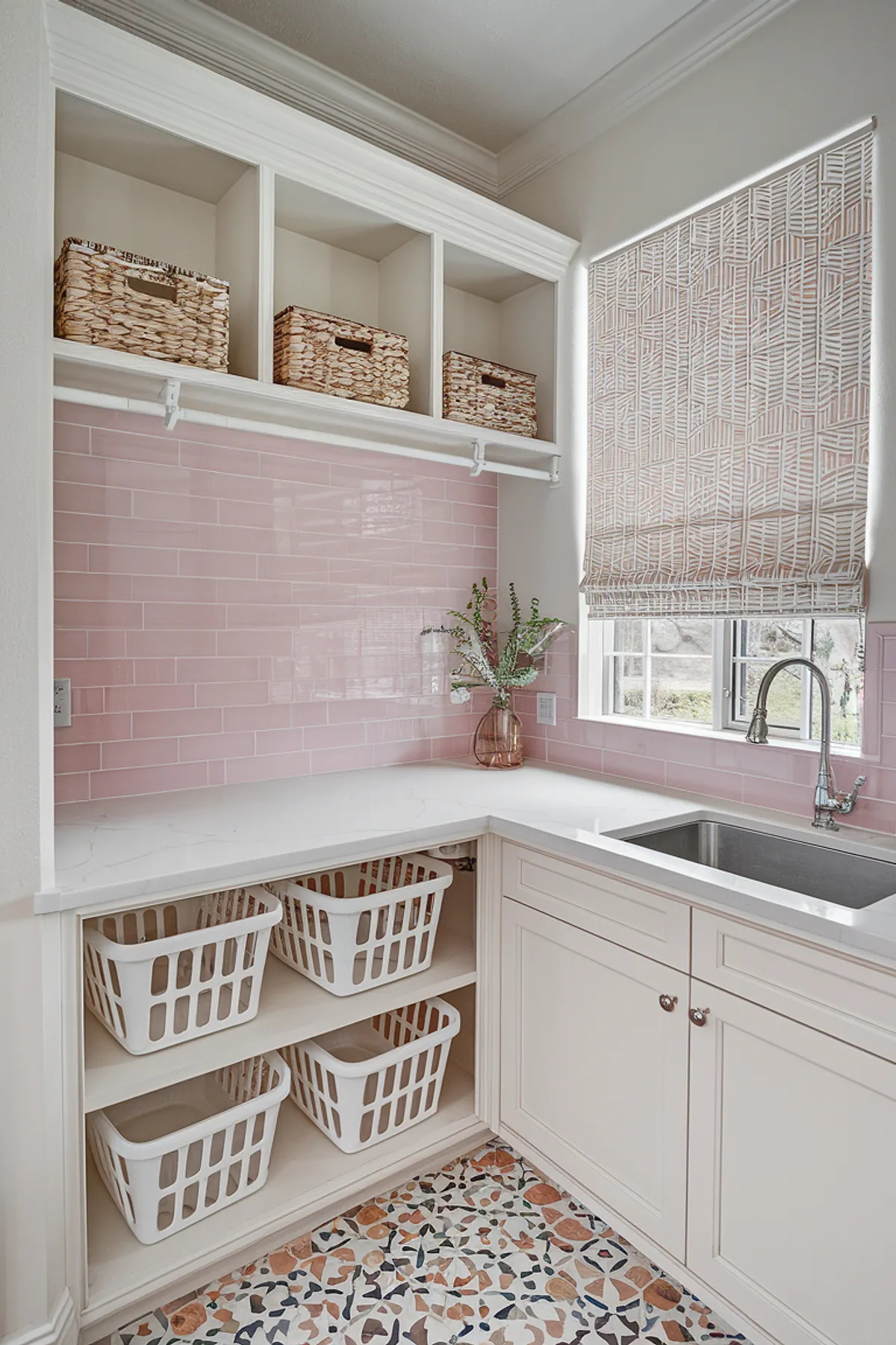 A charming laundry room with pink tiles, organized baskets, and patterned flooring.