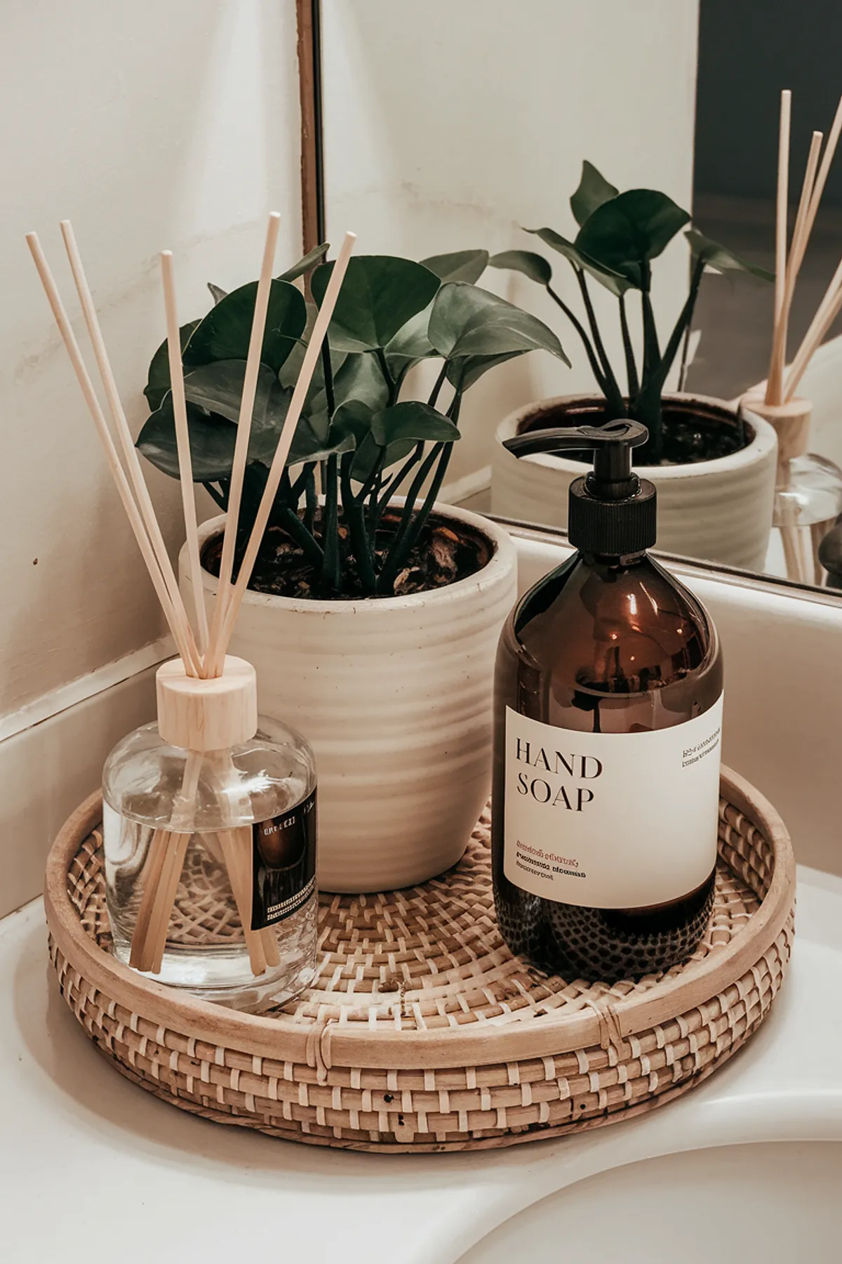 A bathroom counter displaying soap, diffuser, and plants on a woven tray.
