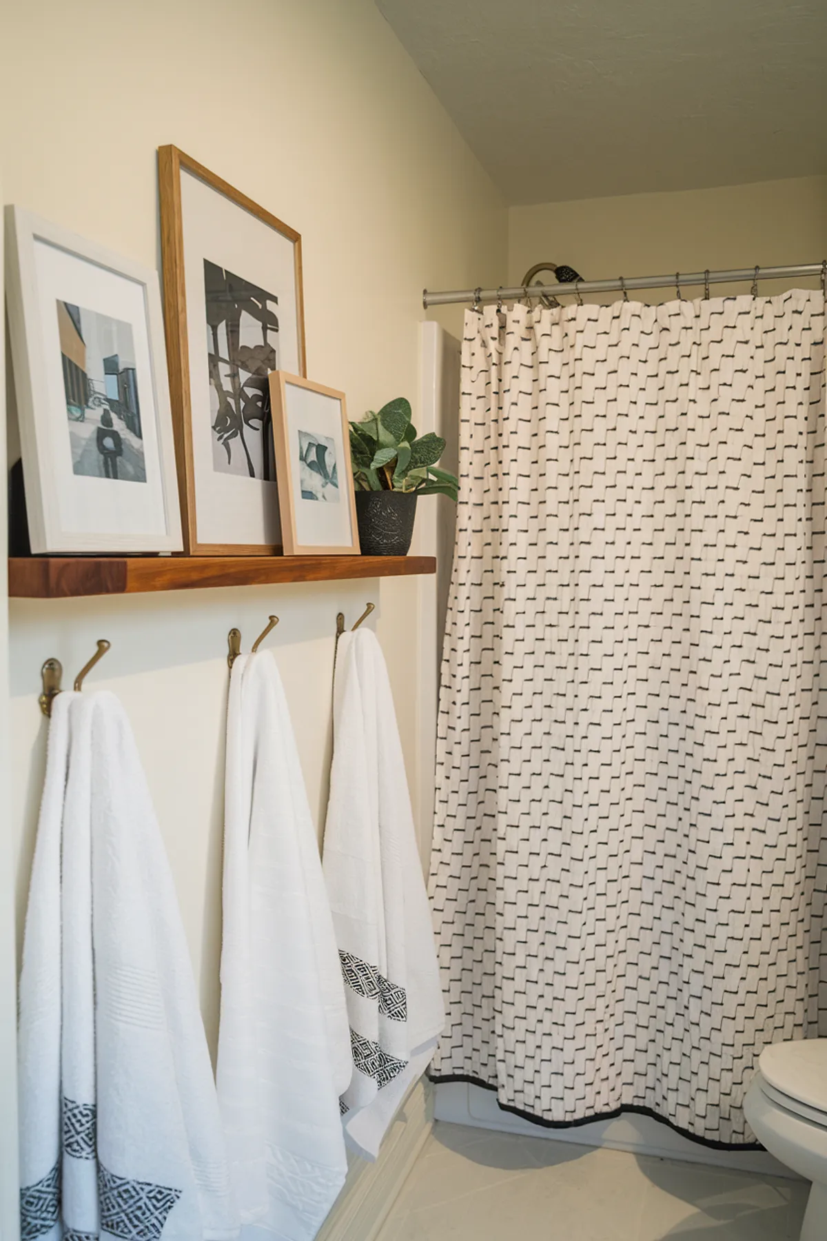 A bathroom featuring framed artwork, patterned shower curtain, and neatly hung towels.