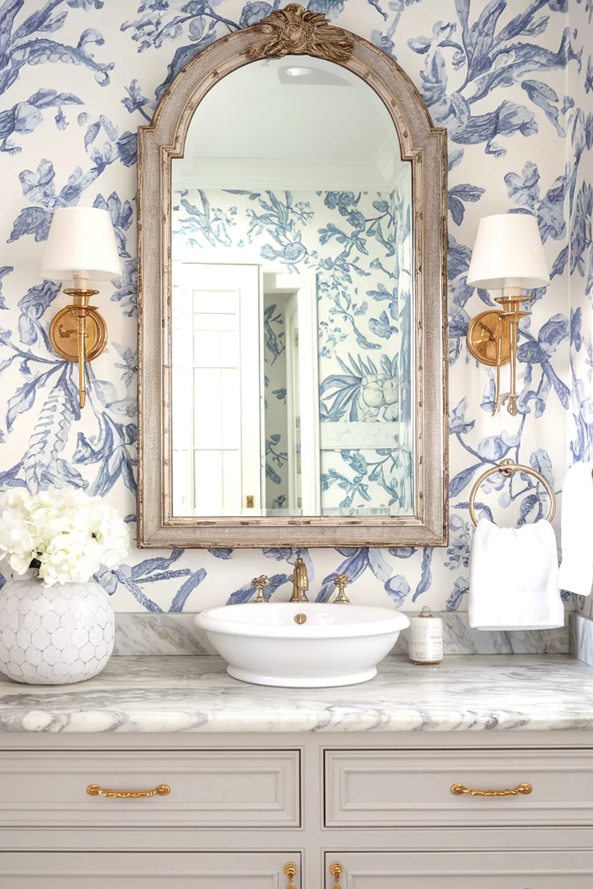A beautifully decorated bathroom with floral wallpaper, a vintage mirror, and stylish sink.