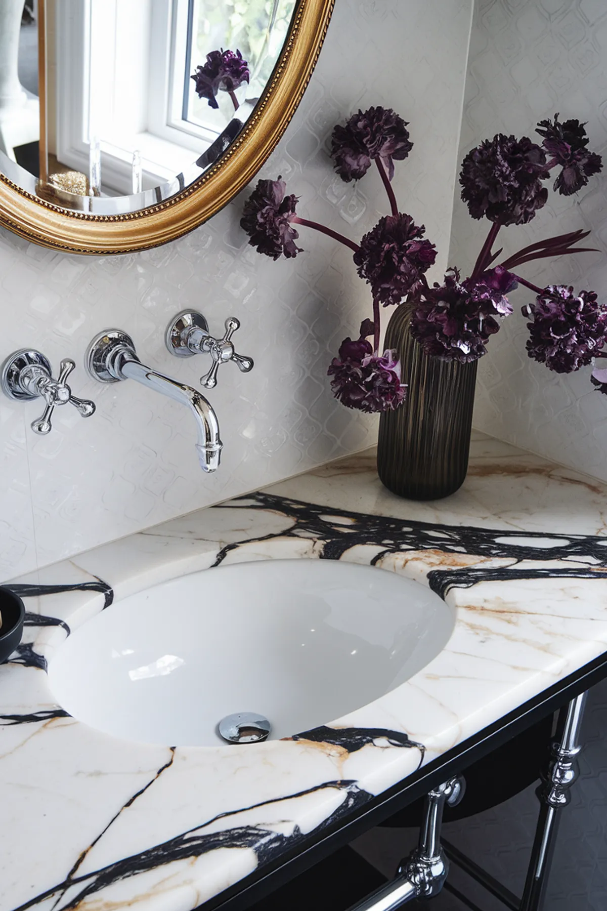 A luxurious bathroom vanity featuring marble countertop, elegant fixtures, and purple flowers in a vase.