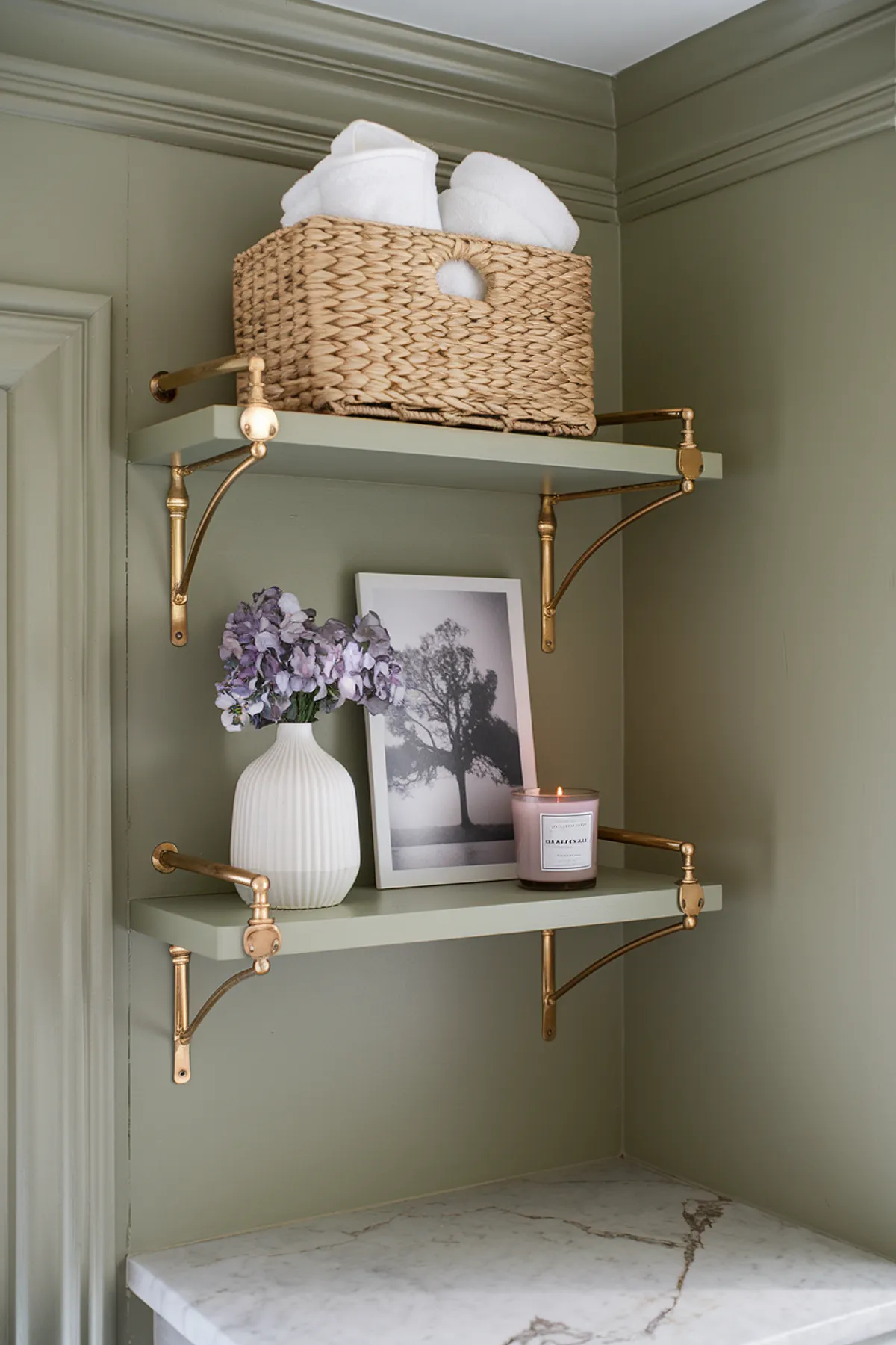 A stylish bathroom shelf displaying towels, flowers, and decorative items against green walls.