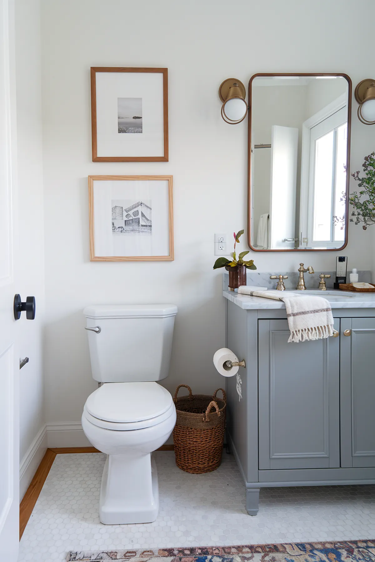 A stylish bathroom featuring gray cabinetry, elegant fixtures, and framed art on the walls.