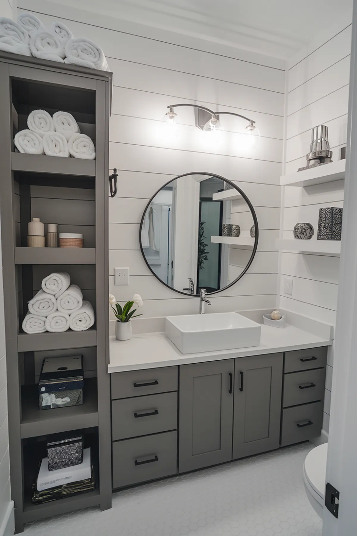 A modern bathroom featuring gray cabinetry, neatly arranged towels, and stylish decor elements.