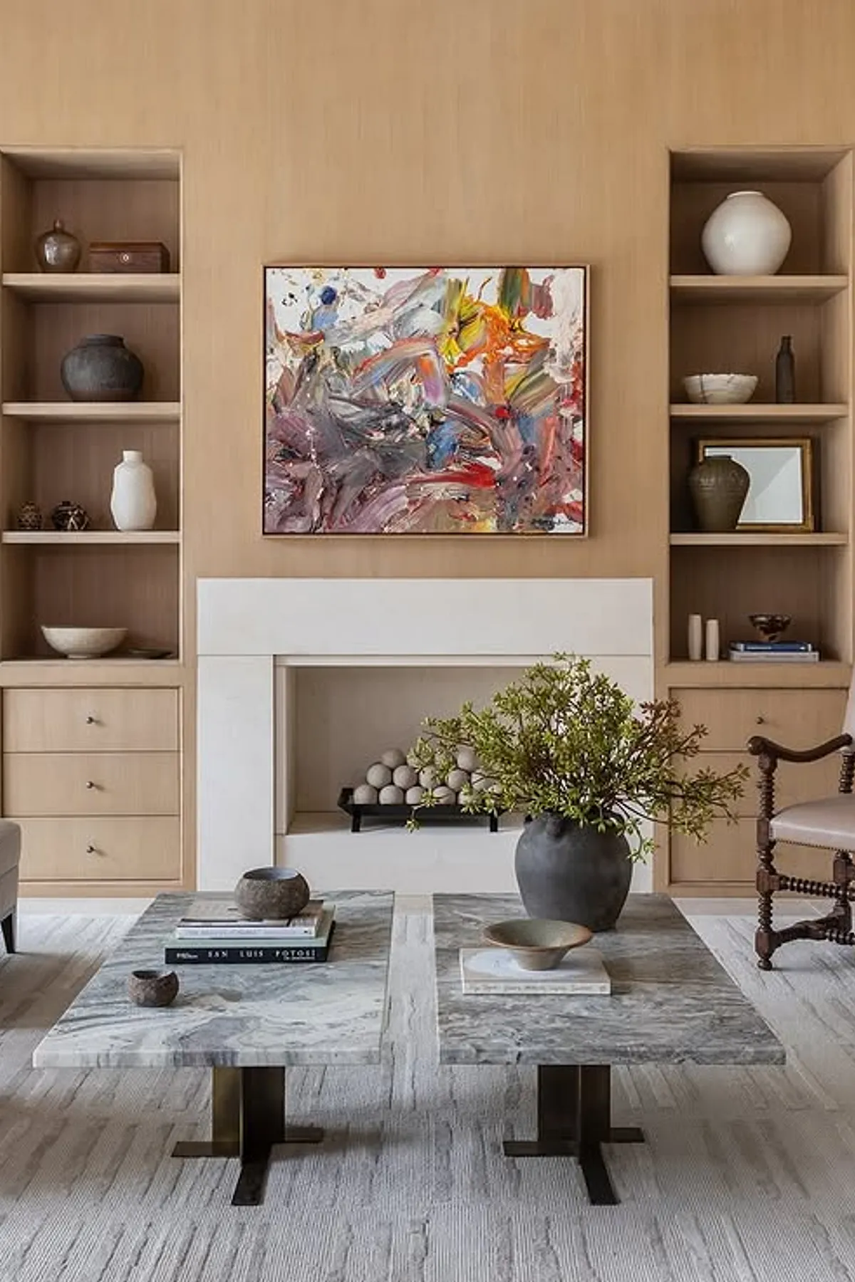 Modern living room featuring wooden shelves, colorful artwork, marble coffee tables, and decorative objects.