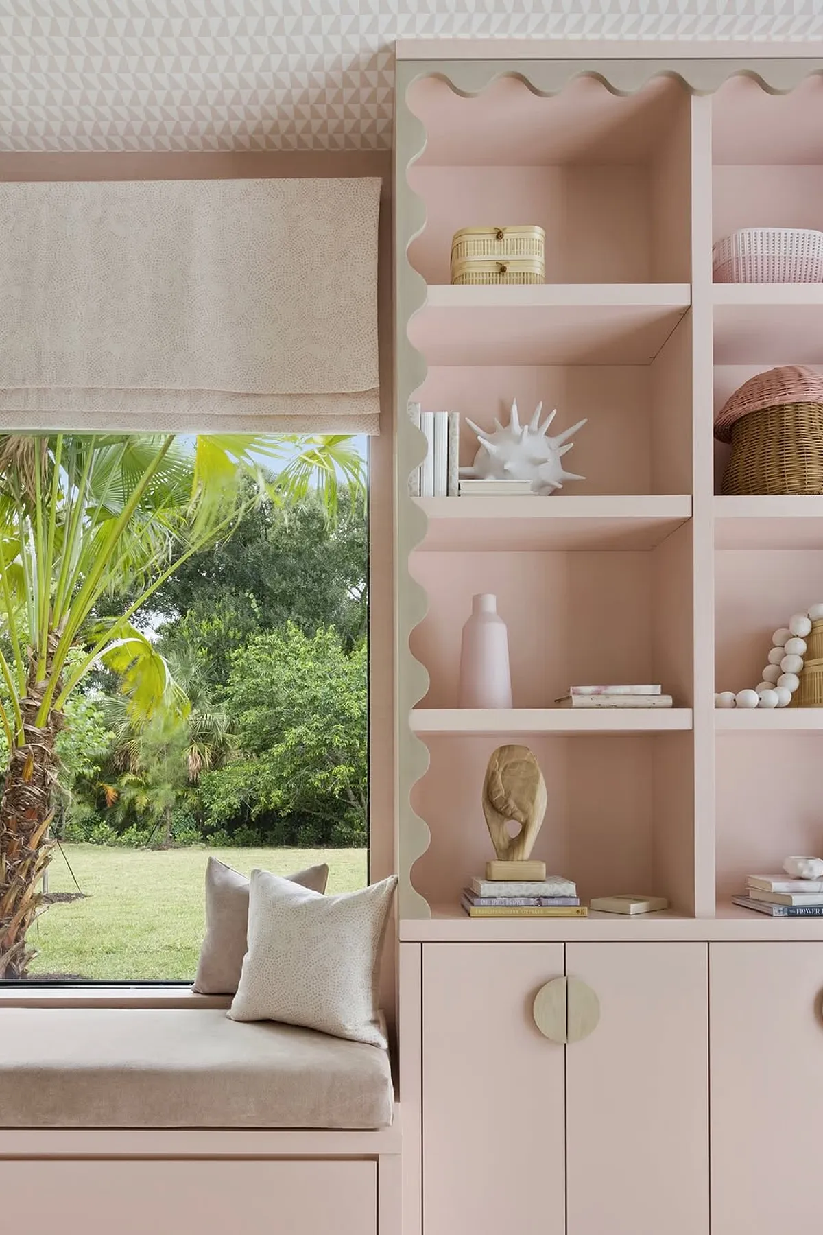 Modern living room featuring pink shelves, textured window seat cushions, decorative objects, and lush greenery outside.