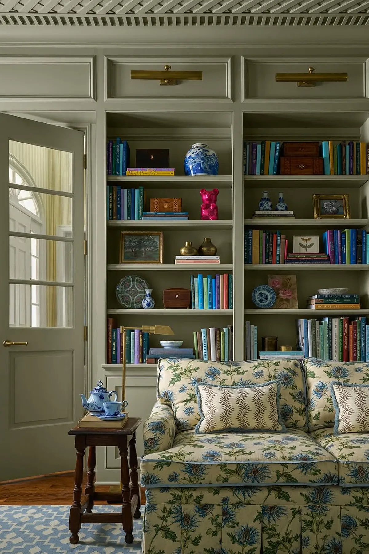 Living room featuring stylish shelving with colorful books, decorative items, floral sofa, and wooden side table.