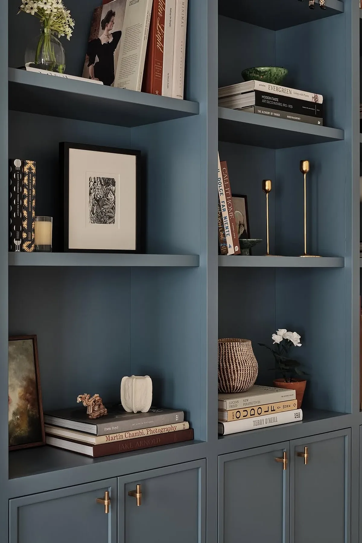 Modern shelf featuring blue background, decorative objects, books, gold candle holders, and potted plants.