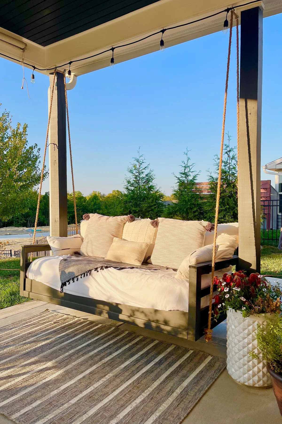 Stylish porch swing with neutral cushions and decorative pillows, suspended in a lush garden setting.