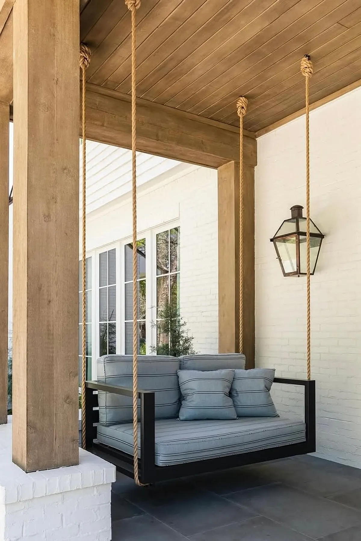 A modern porch swing featuring blue cushions and a wooden frame, suspended from natural wood beams.