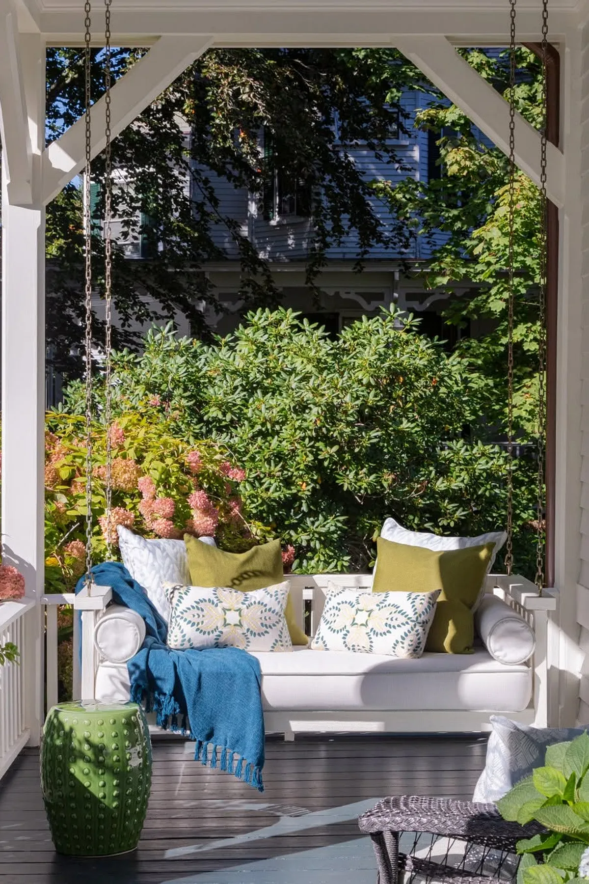 A charming porch swing with colorful cushions, a blue throw, and green garden views in the background.