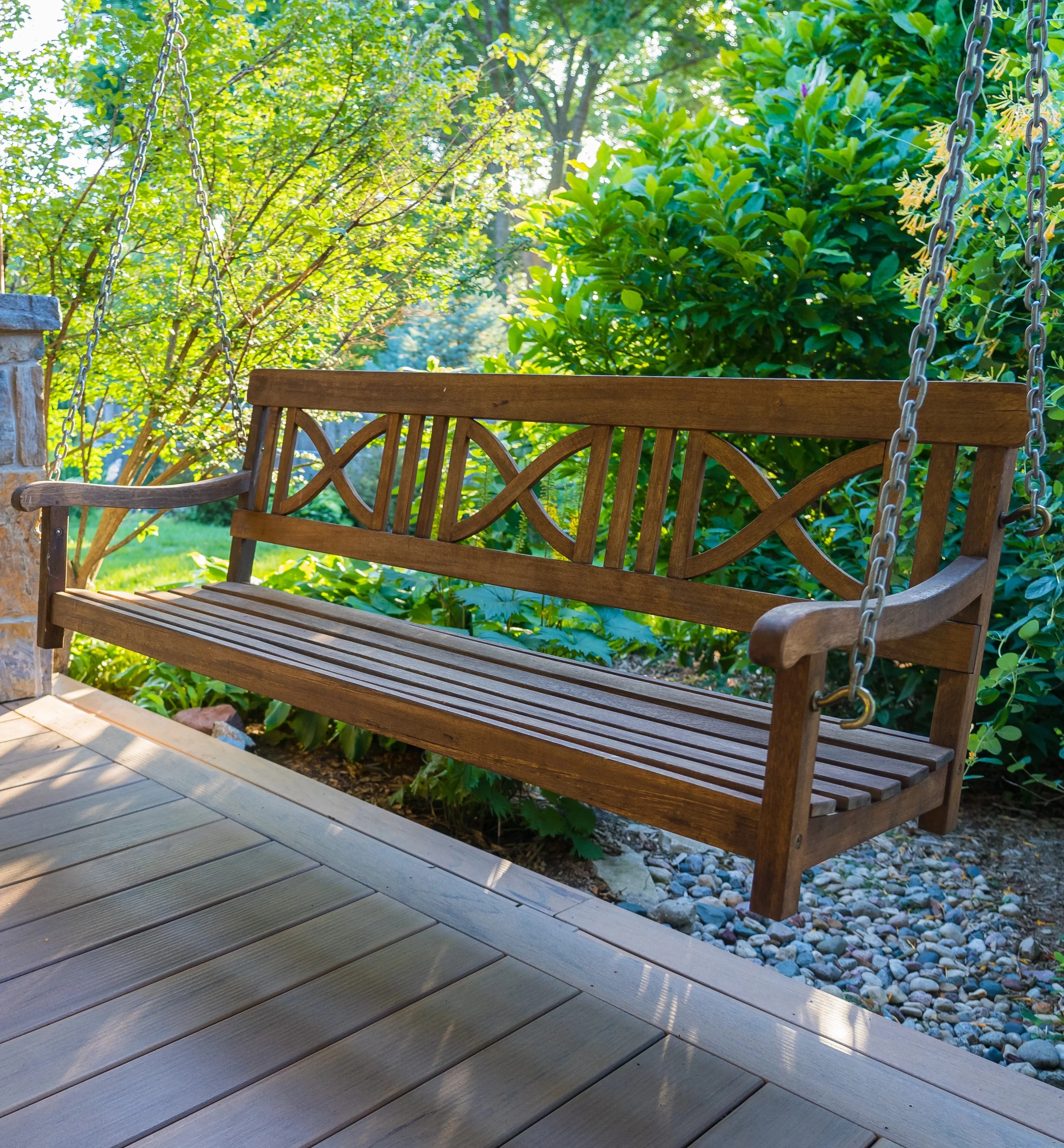 Wooden porch swing featuring an intricate design, suspended in a lush garden setting