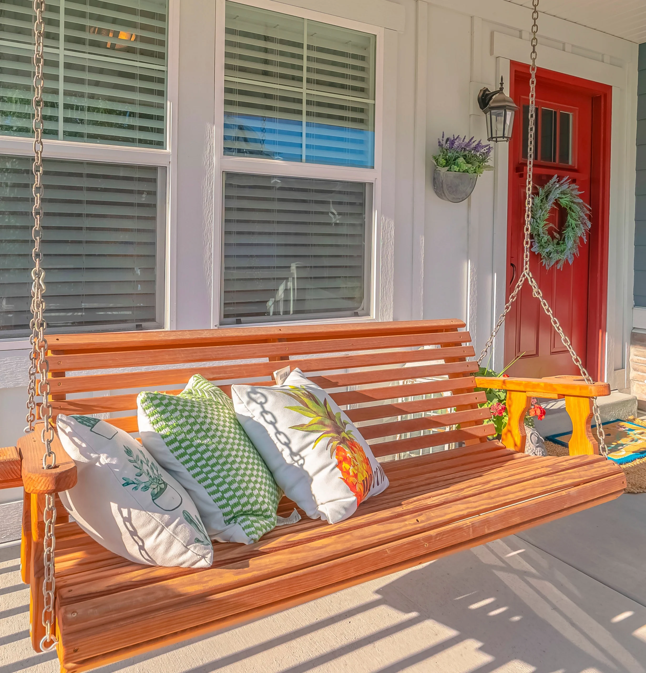 Colorful porch swing with patterned pillows, set against a bright red door and sunny windows