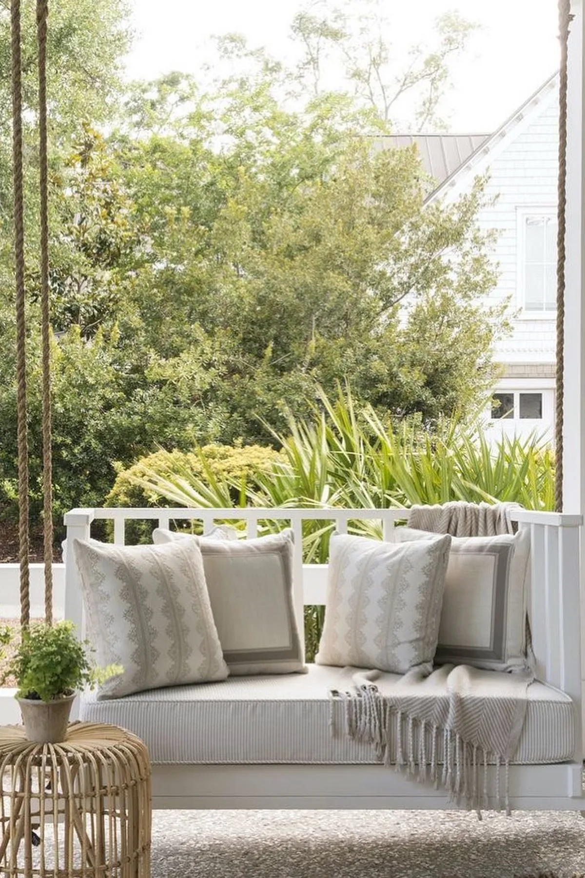 A white porch swing with gray patterned pillows, accented by a small plant and textured throw.