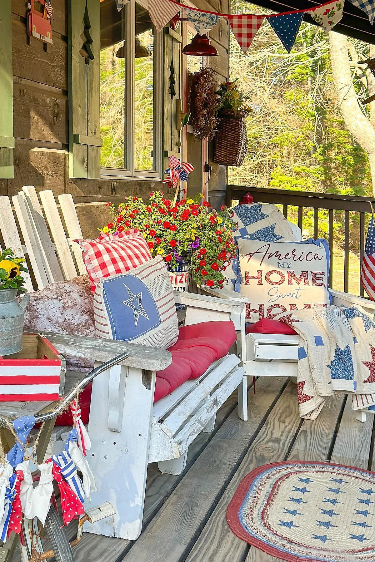 A cozy porch featuring white Adirondack chairs adorned with patriotic pillows, colorful flowers, and festive decor.