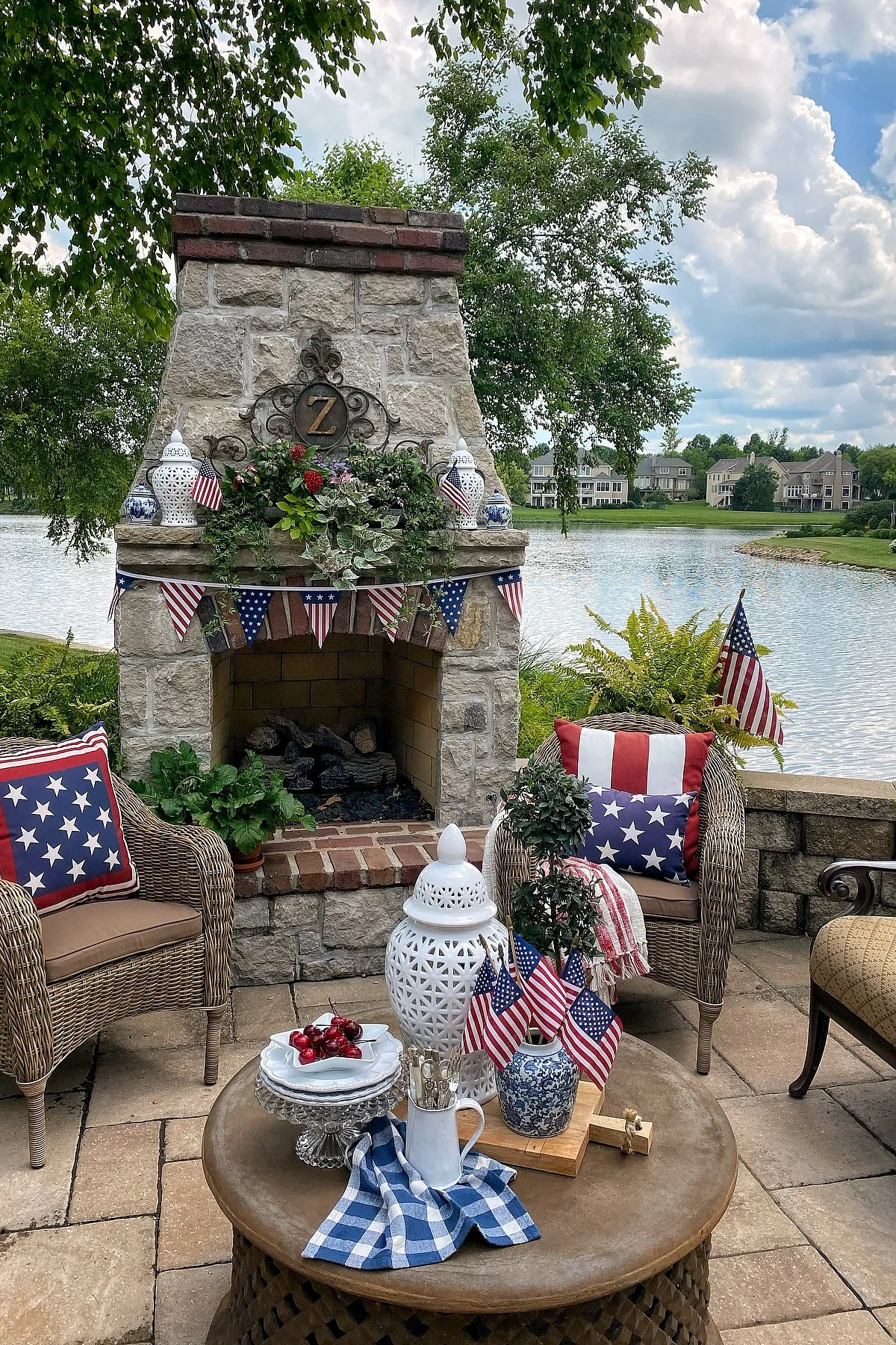 A cozy outdoor area featuring a stone fireplace adorned with greenery, patriotic flags, and themed cushions.