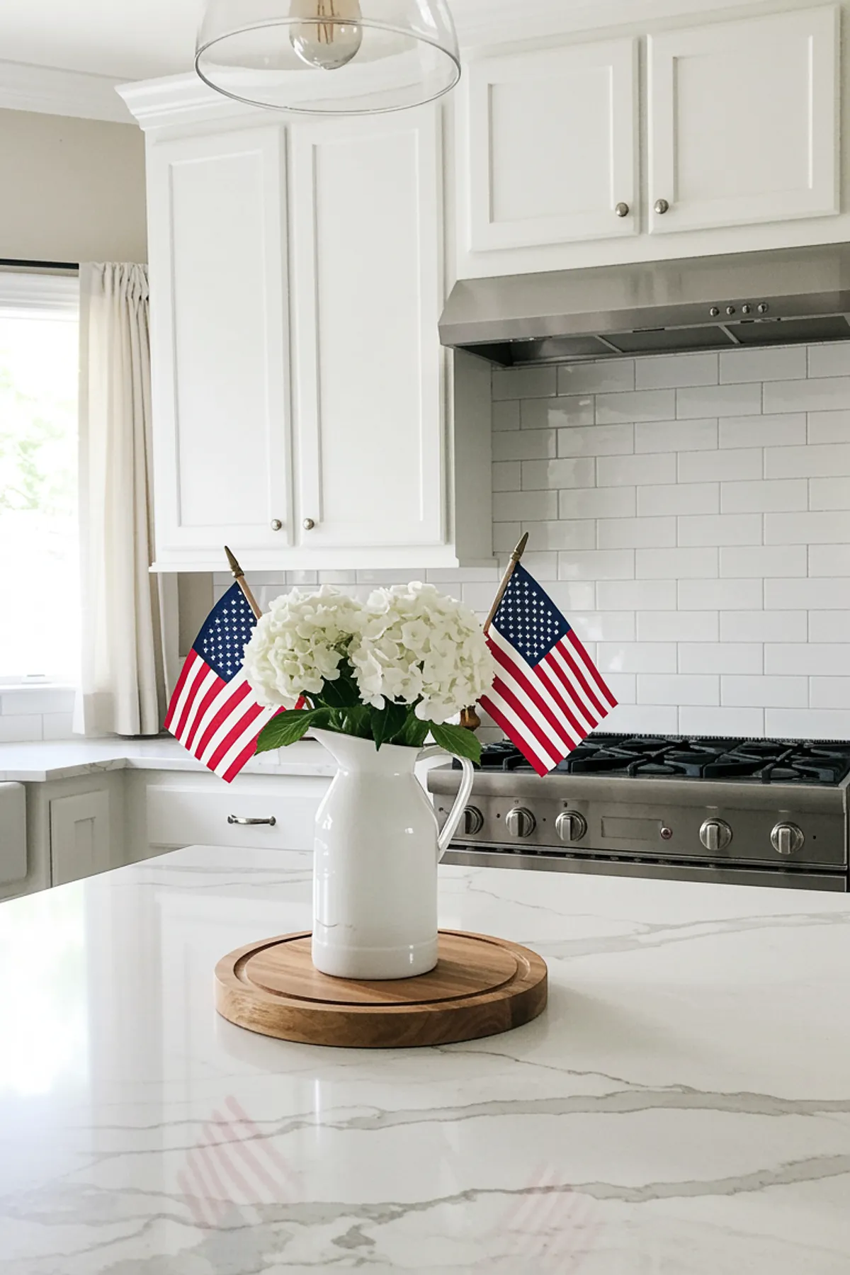A kitchen island featuring white hydrangeas in a pitcher, two American flags, and a marble countertop.