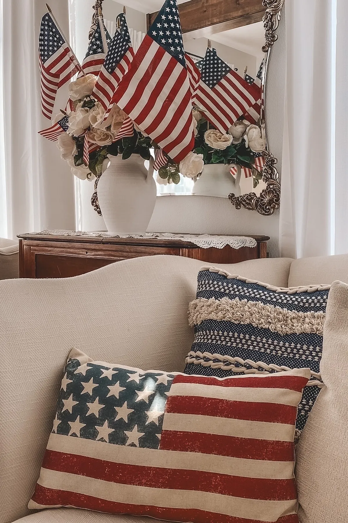 A living room featuring American flags in a vase, white flowers, and patterned pillows on a neutral sofa.