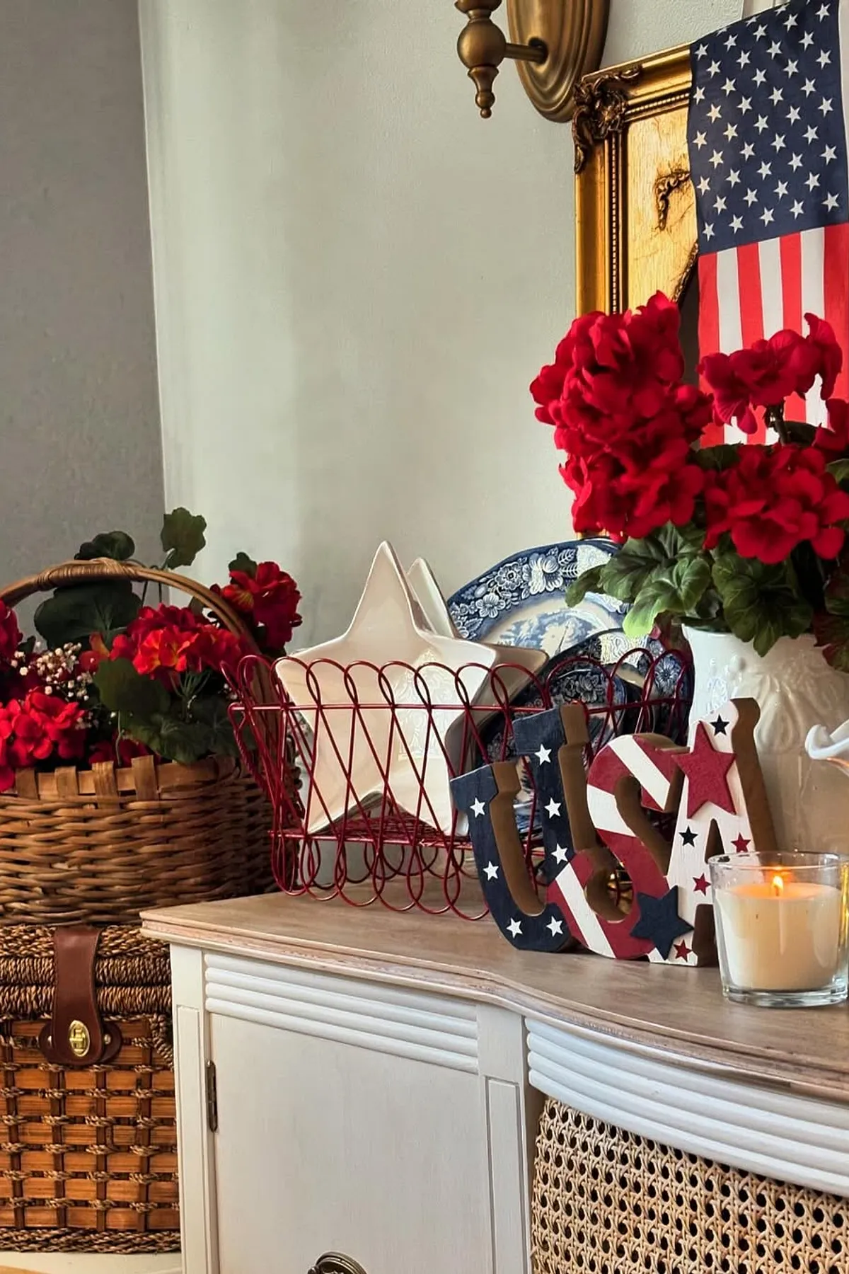 A decorative console table featuring red flowers, star-shaped dishes, a USA wooden sign, and candles.